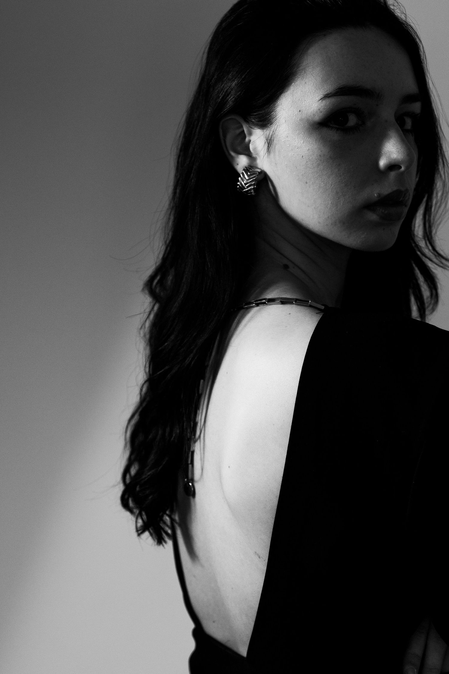 Black and white portrait of young woman with long dark hair showing bare back in studio.