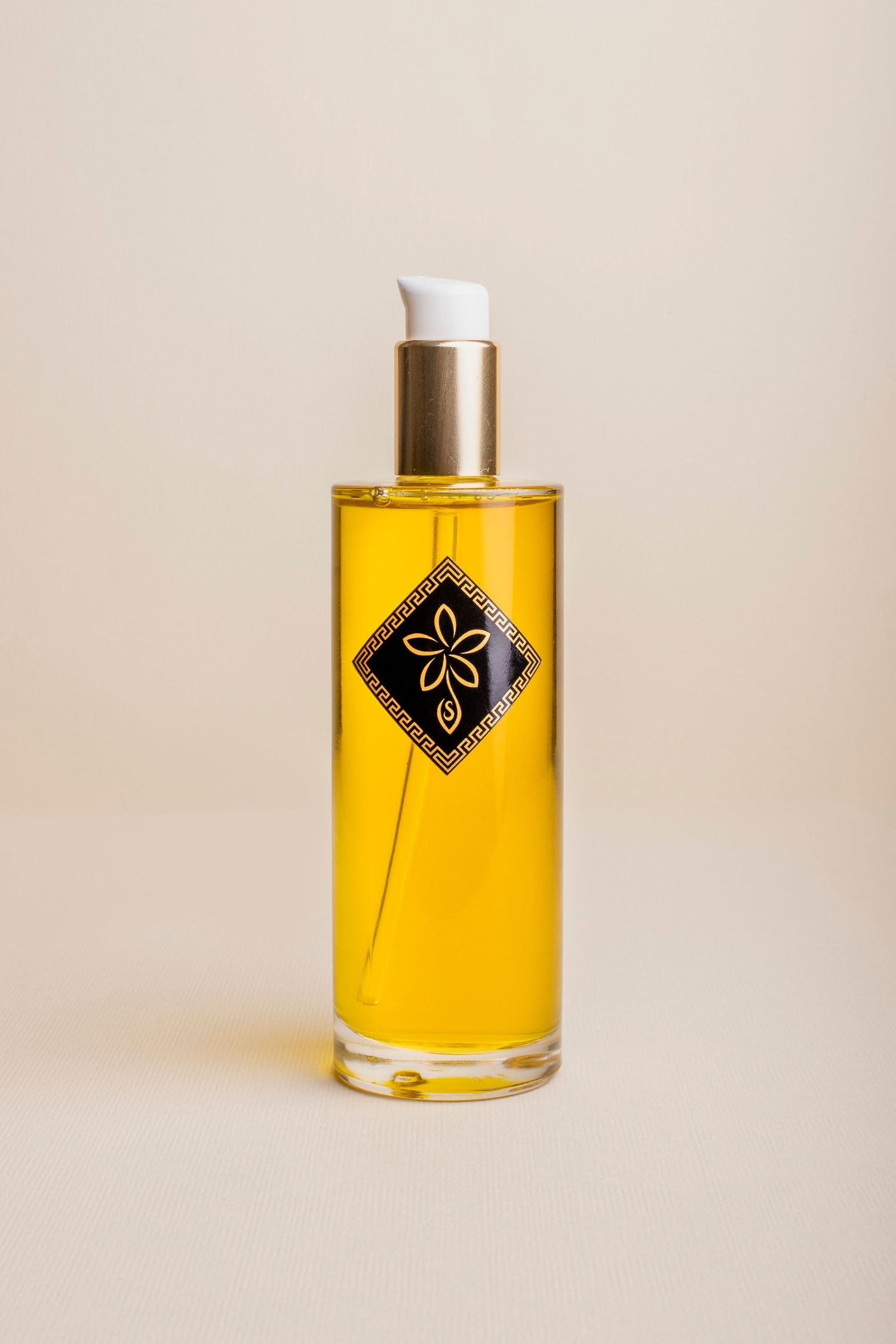 Elegant glass bottle of golden beauty oil with black diamond label on neutral beige background.