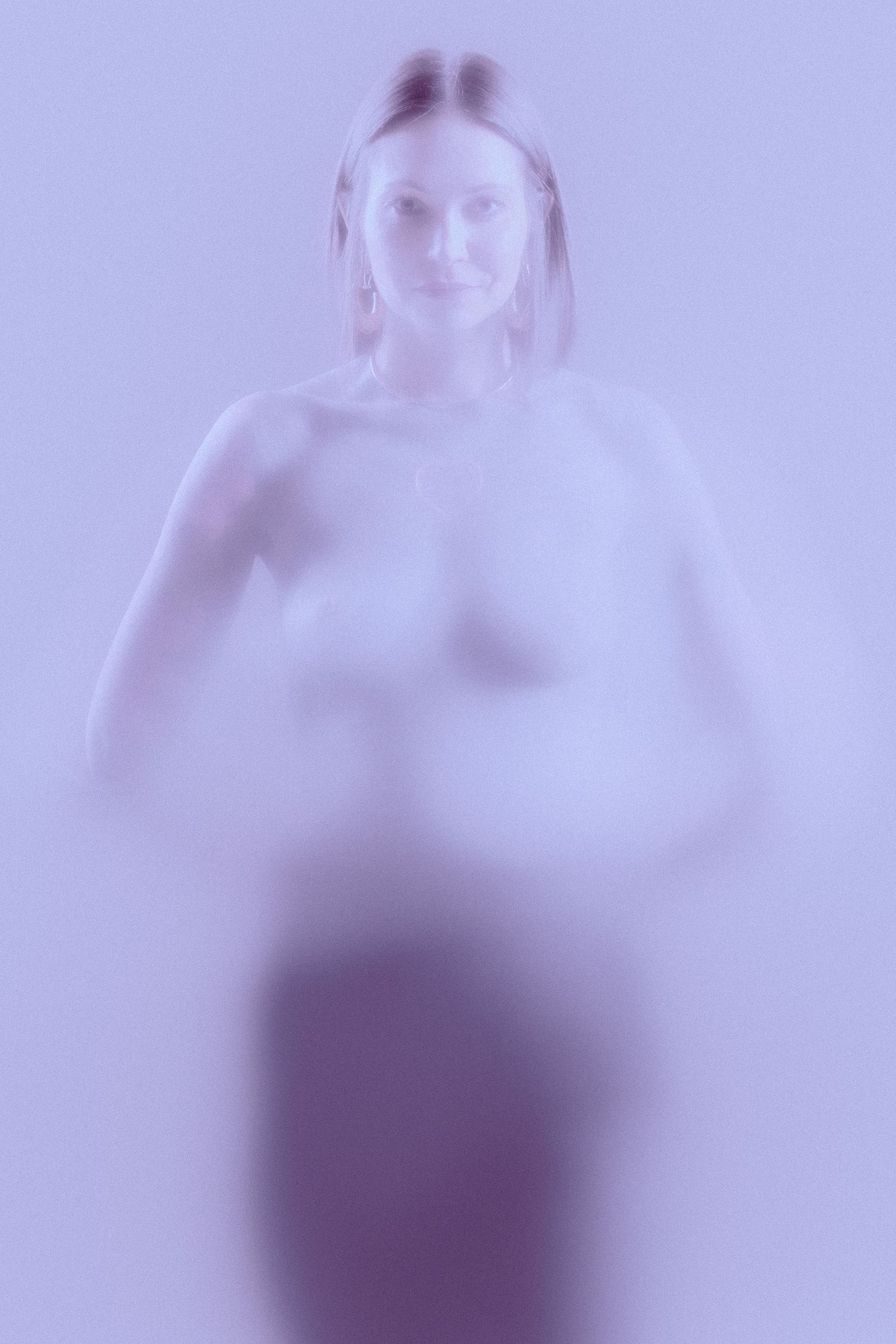 Soft purple-toned diffused portrait of a woman standing in ethereal misty light.