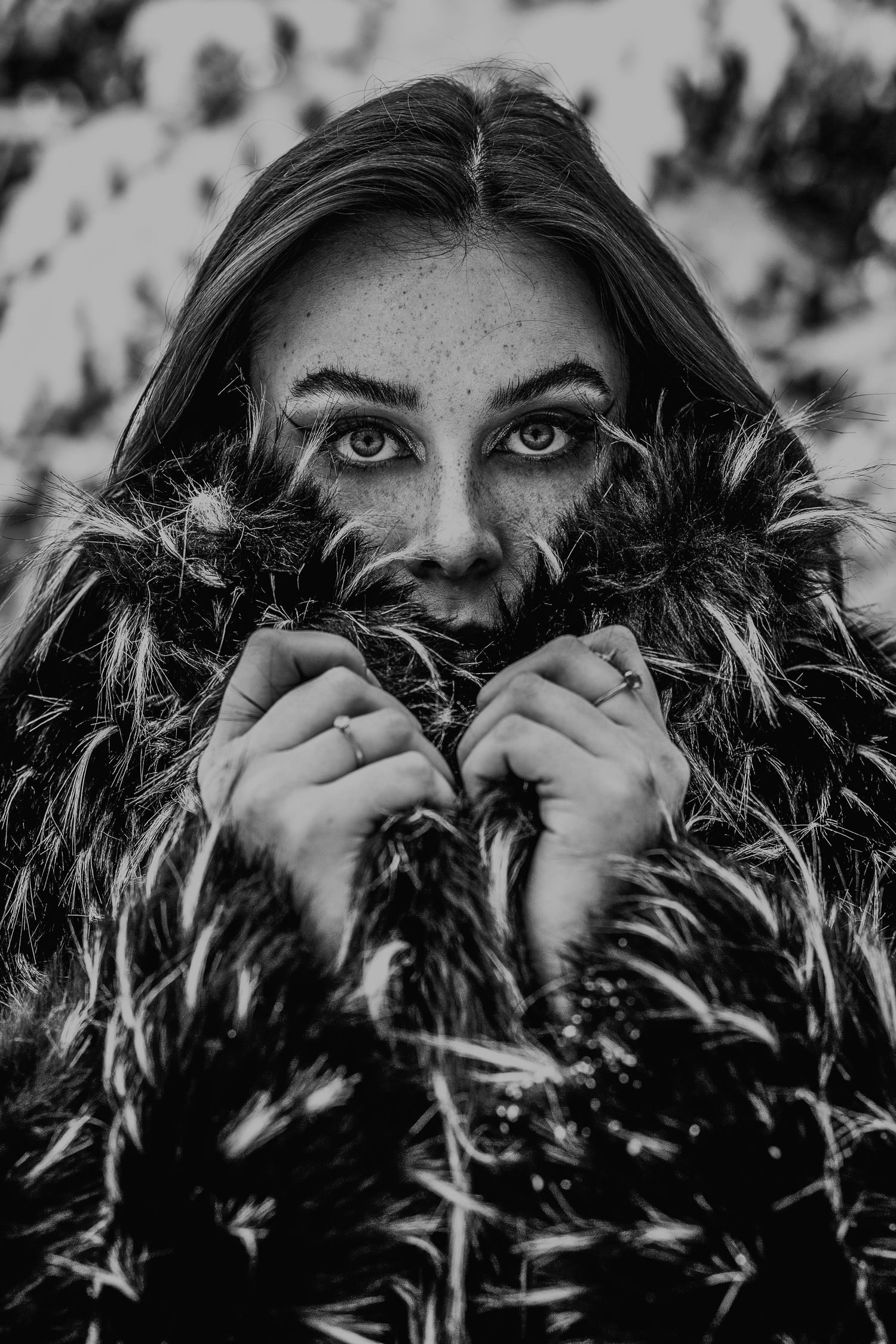 Black and white close-up portrait of a freckled woman with striking eyes wrapped in a fur coat.