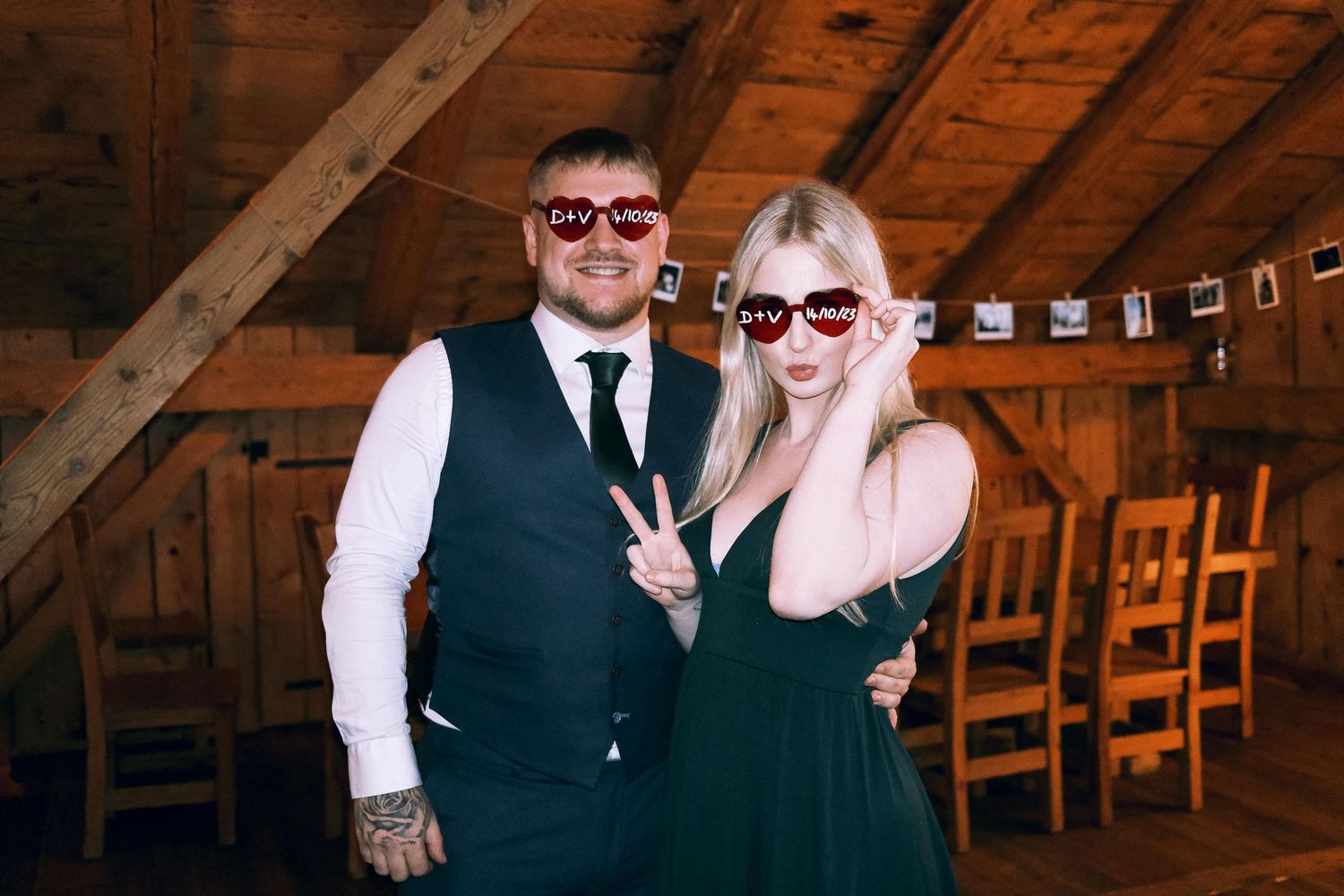 Couple poses with heart-shaped novelty sunglasses at rustic barn wedding reception.