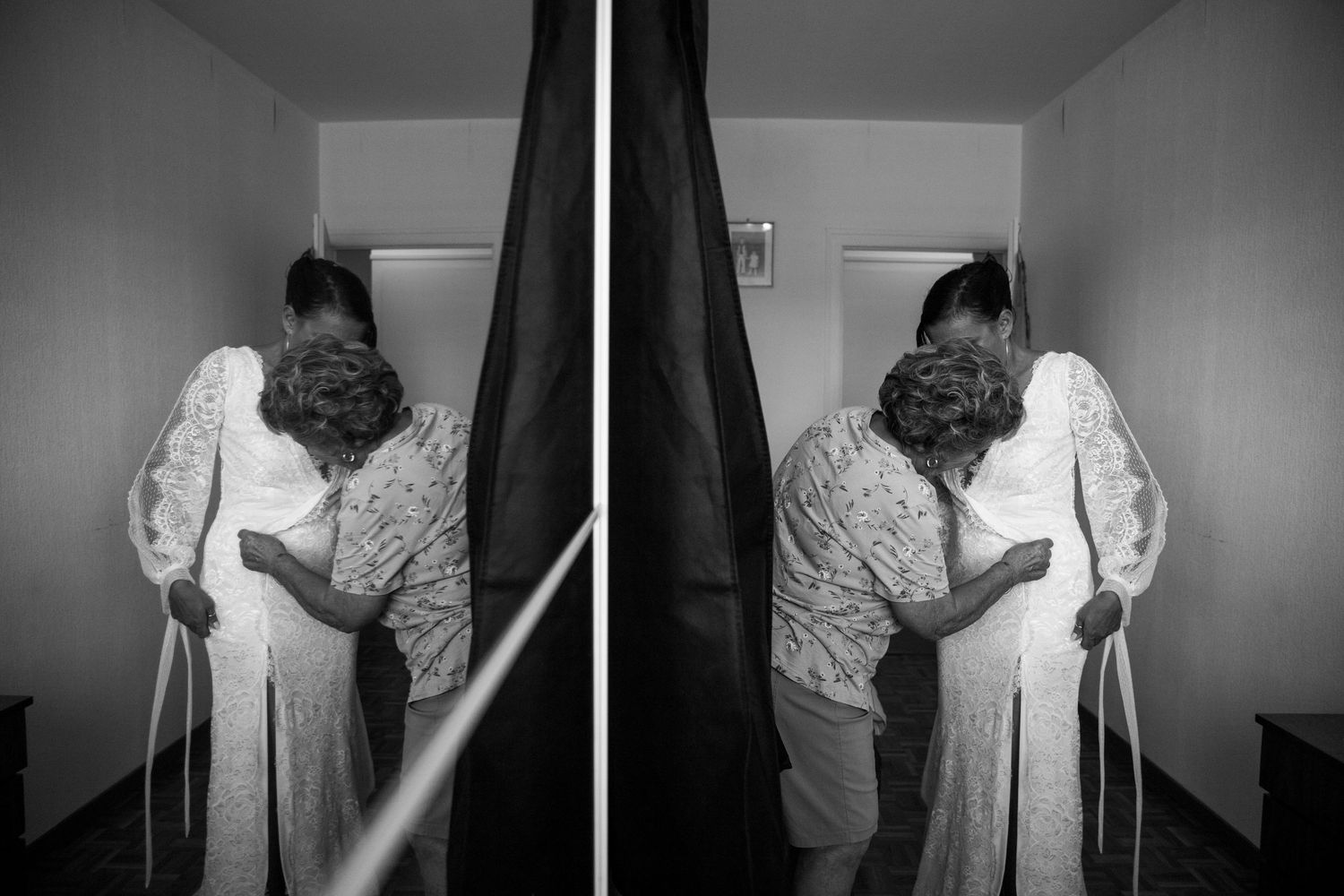 A black and white mirrored image of a bride in a white lace gown standing in a hallway.