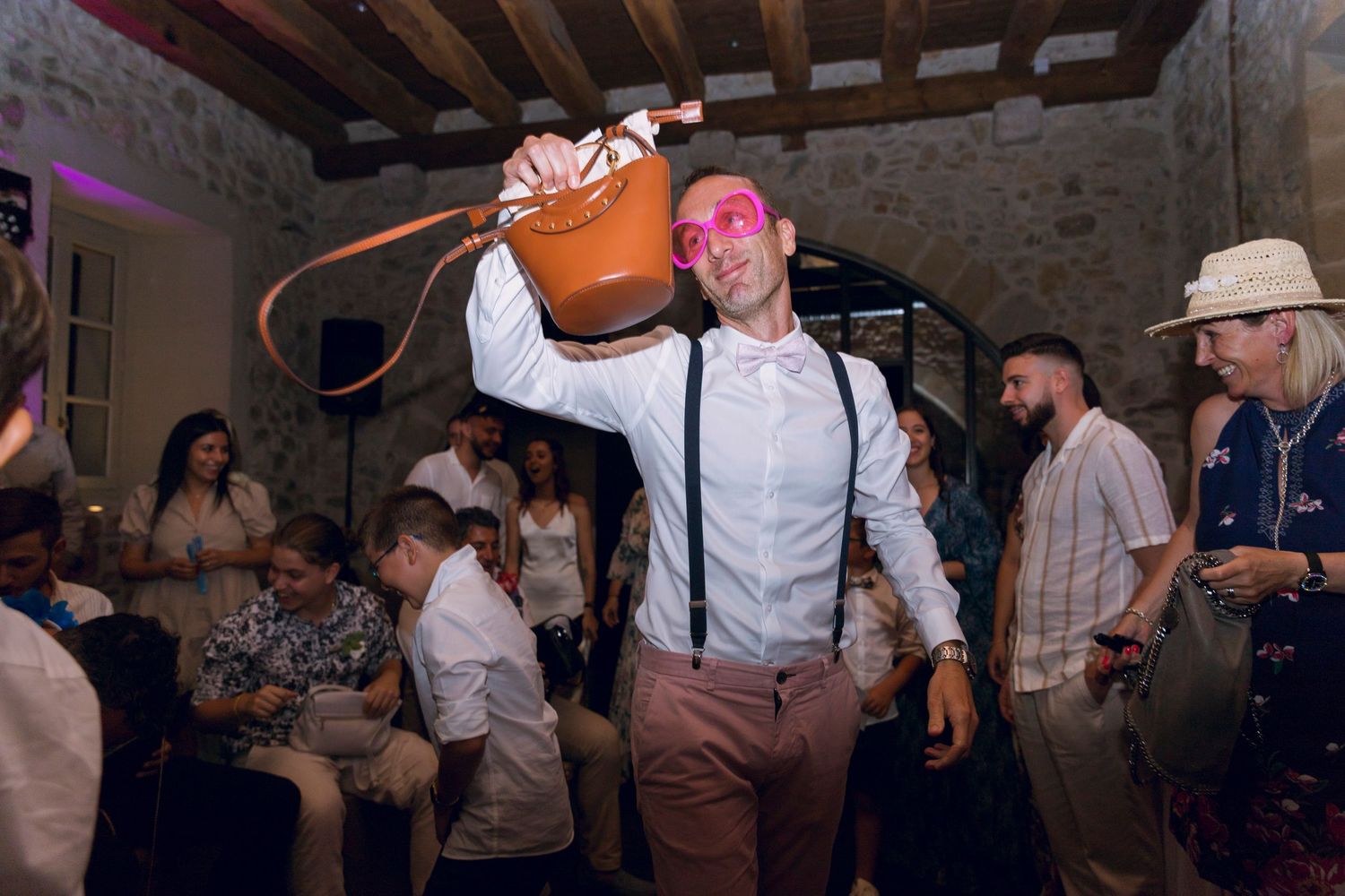 Man in suspenders holding copper bucket aloft at lively wedding reception party.