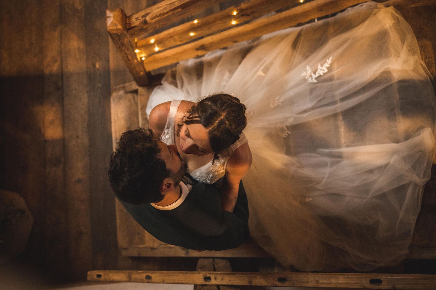 Aerial view of bride and groom sharing a kiss under wedding veil indoors.