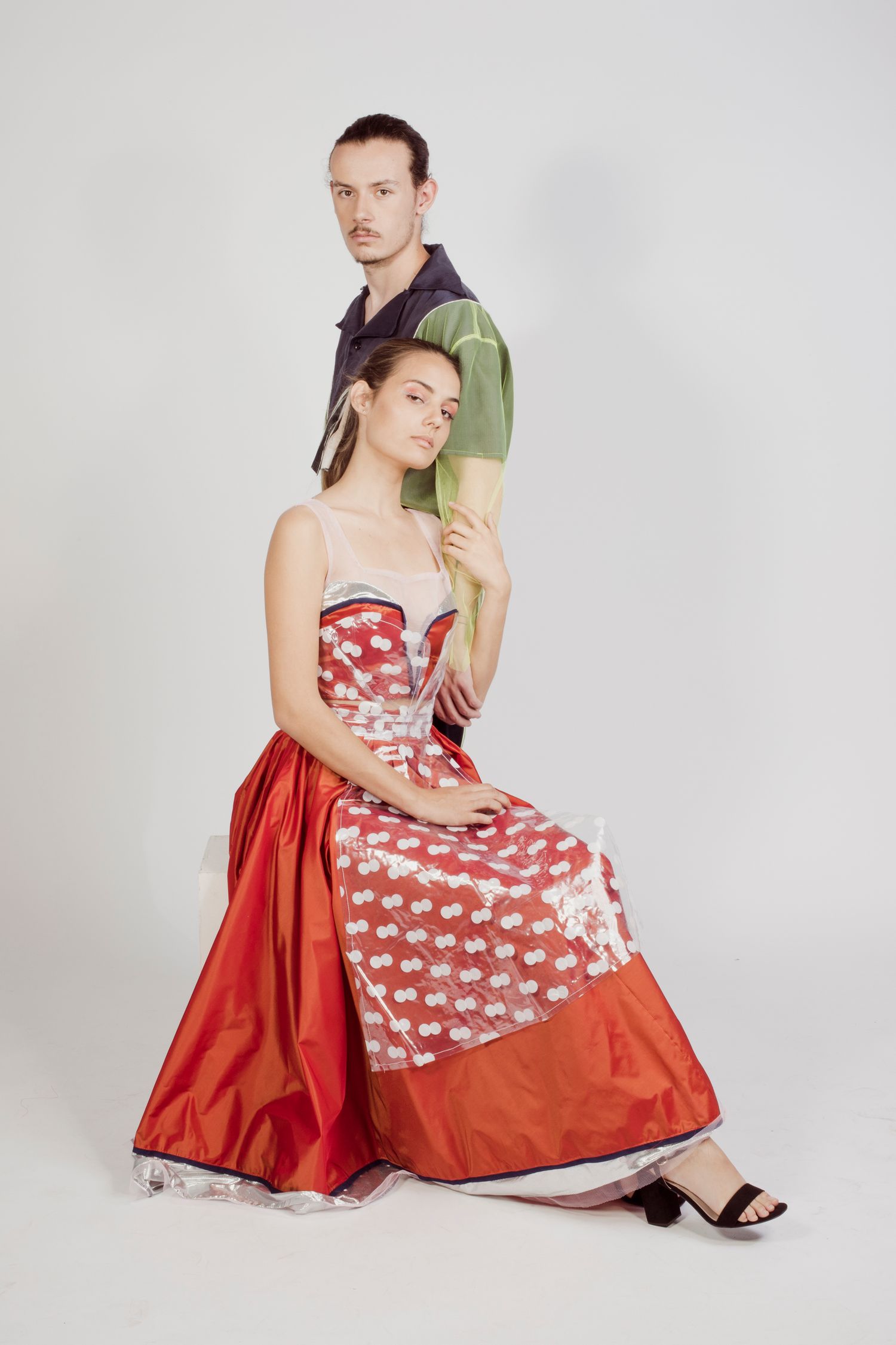 A woman in a red floral gown sits as a man in a dark shirt poses behind her.