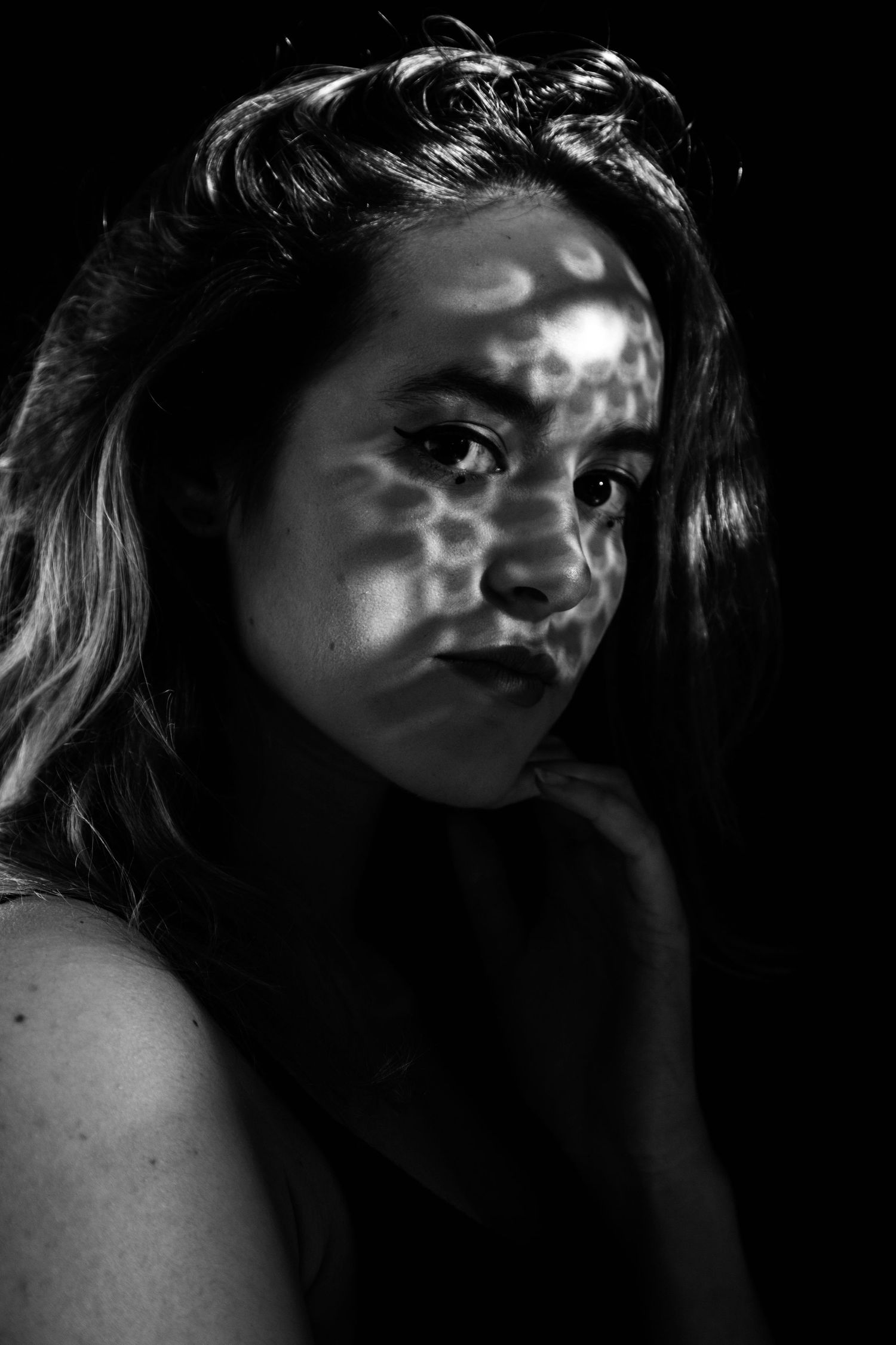 Dramatic black and white portrait of a young woman with dappled light shadows across her face.