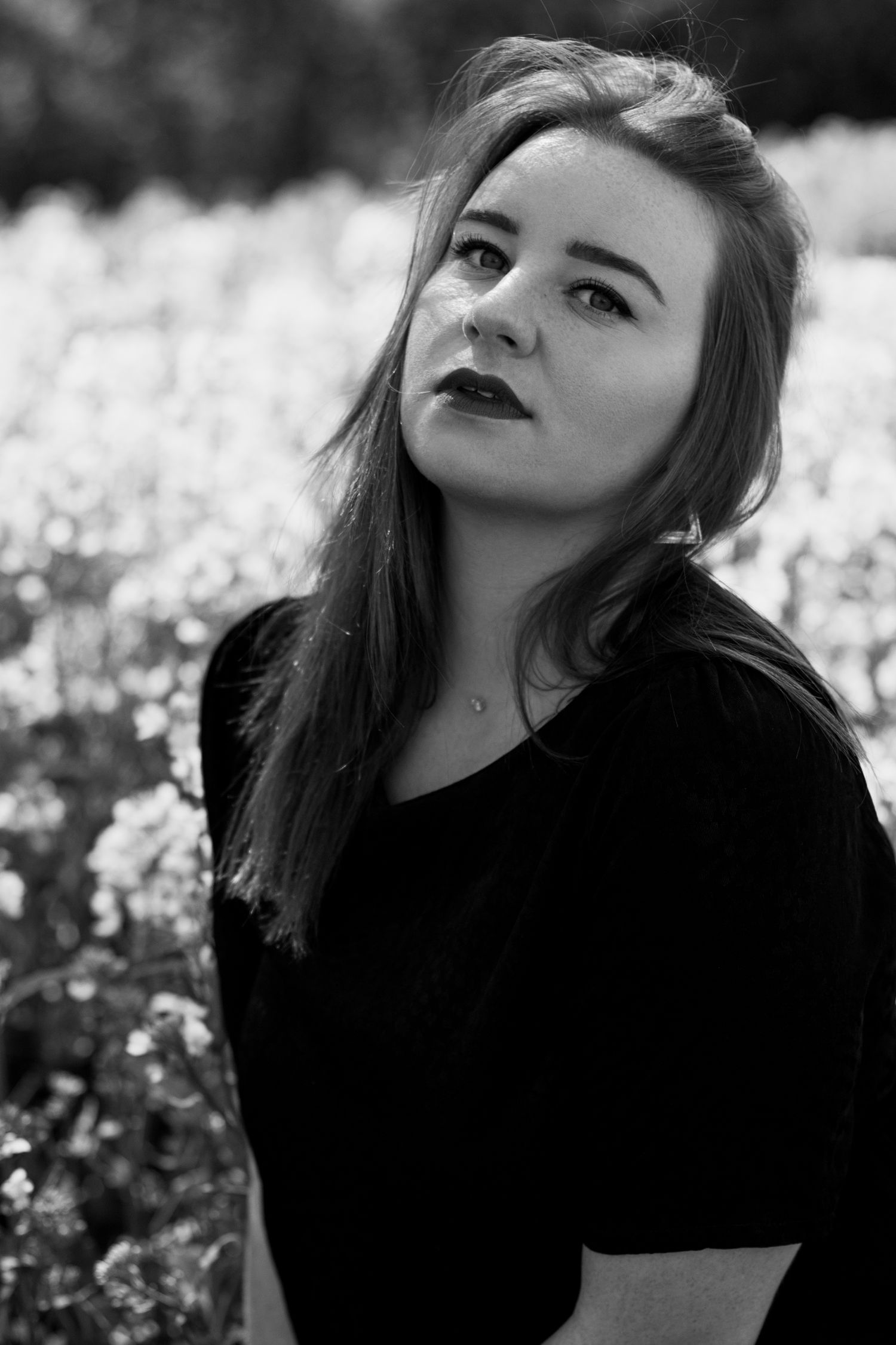 Black and white portrait of a young woman with long hair gazing upward in a flower field.
