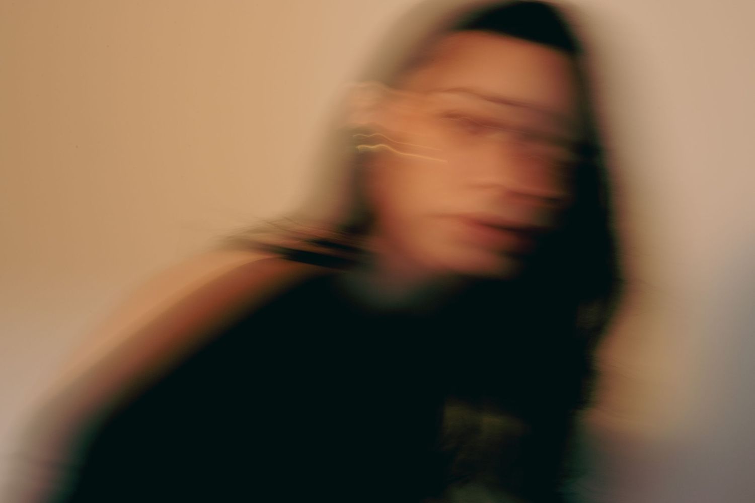 Artistic blurred motion portrait of woman with dark hair against beige background.