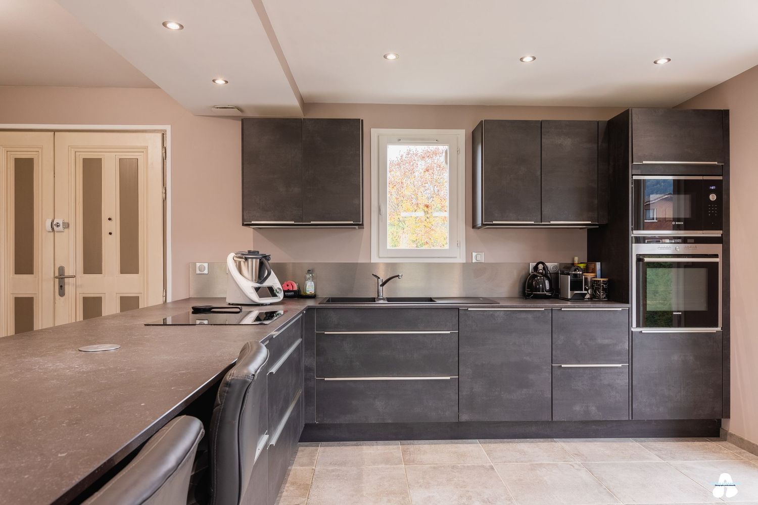 Contemporary grey kitchen with built-in appliances, dark stone countertops and tile flooring.