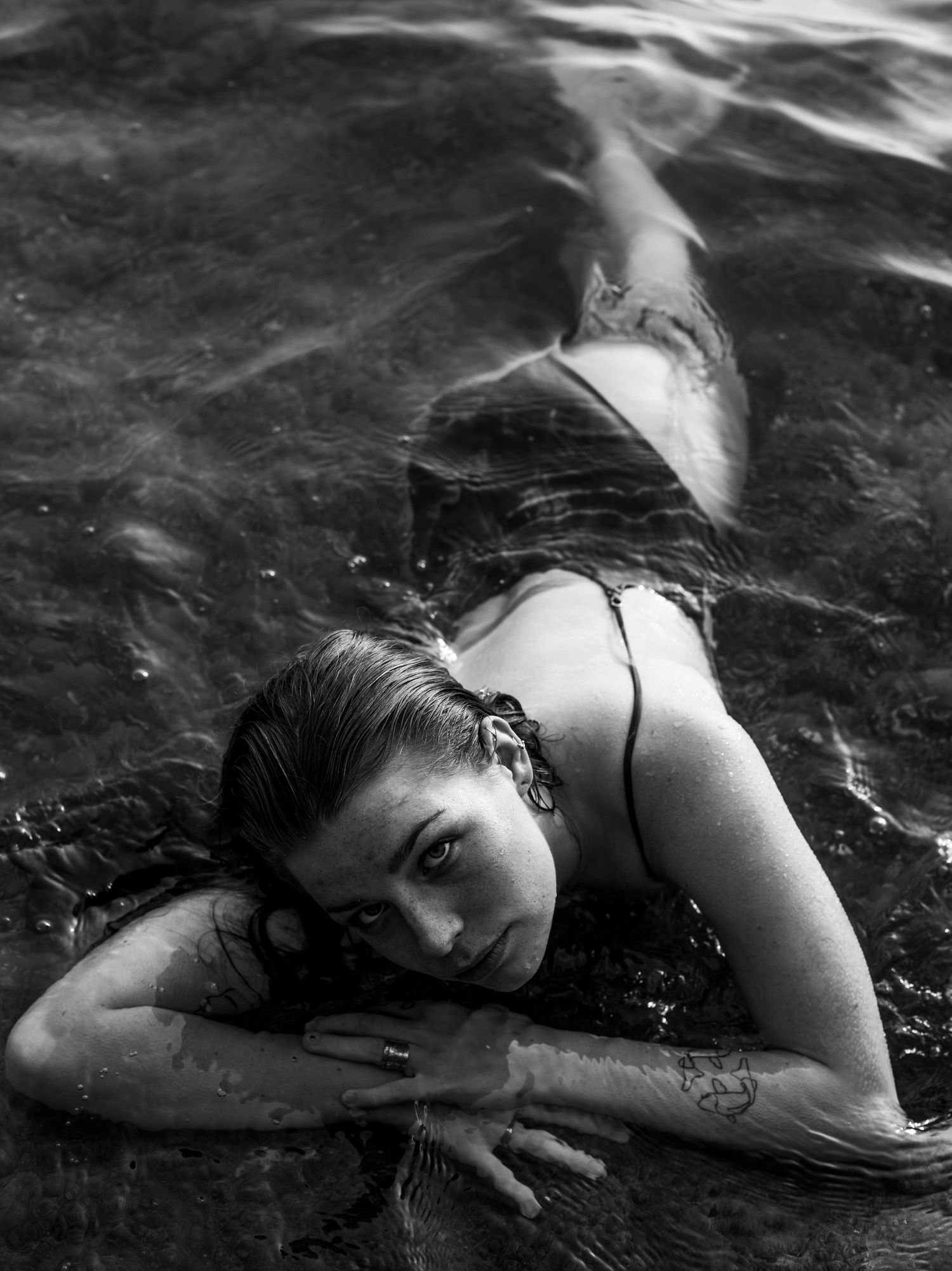 Black and white photo of a woman lying in shallow water wearing a bikini.