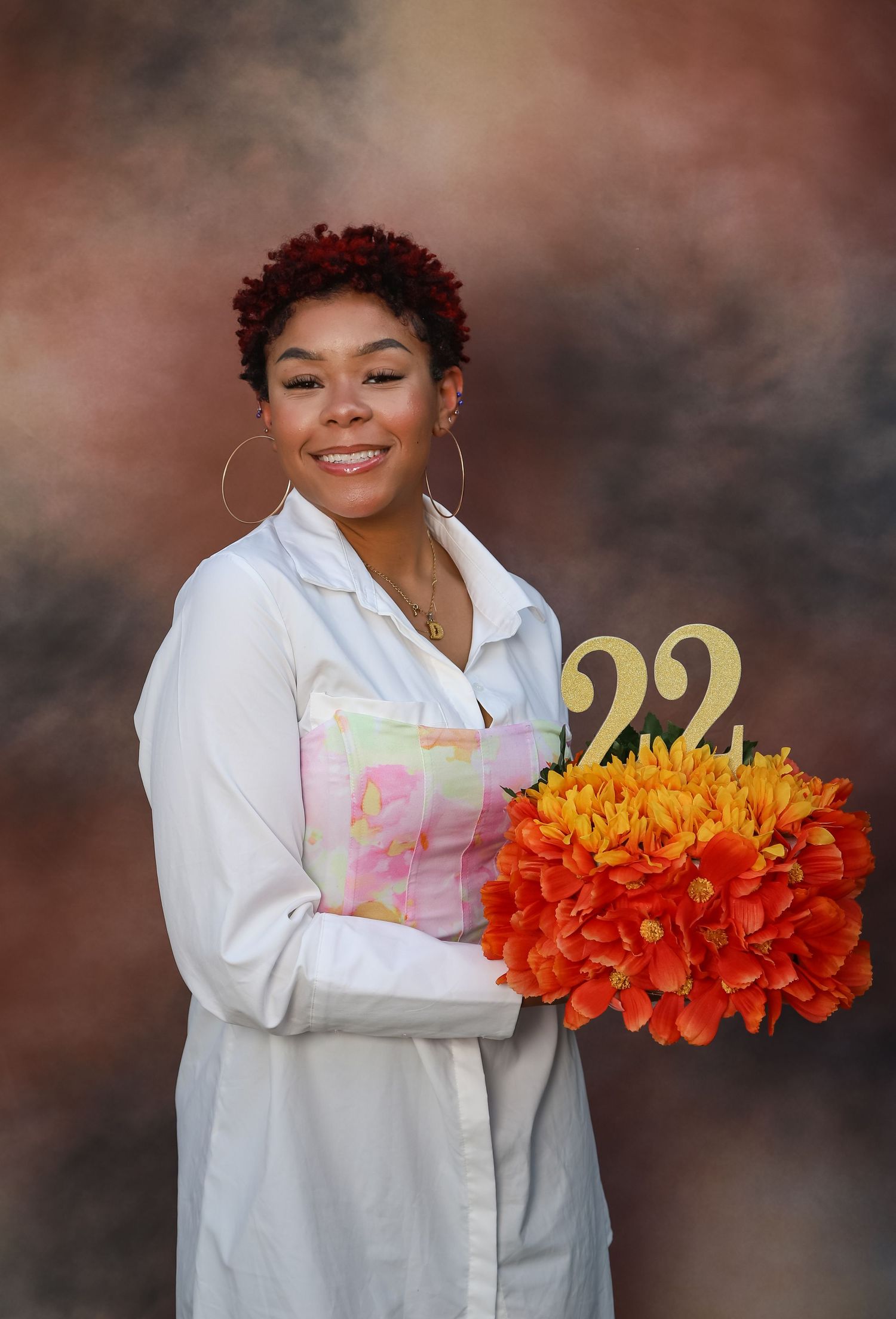 Smiling young woman in white coat holding orange flowers with a gold number 22 decoration.