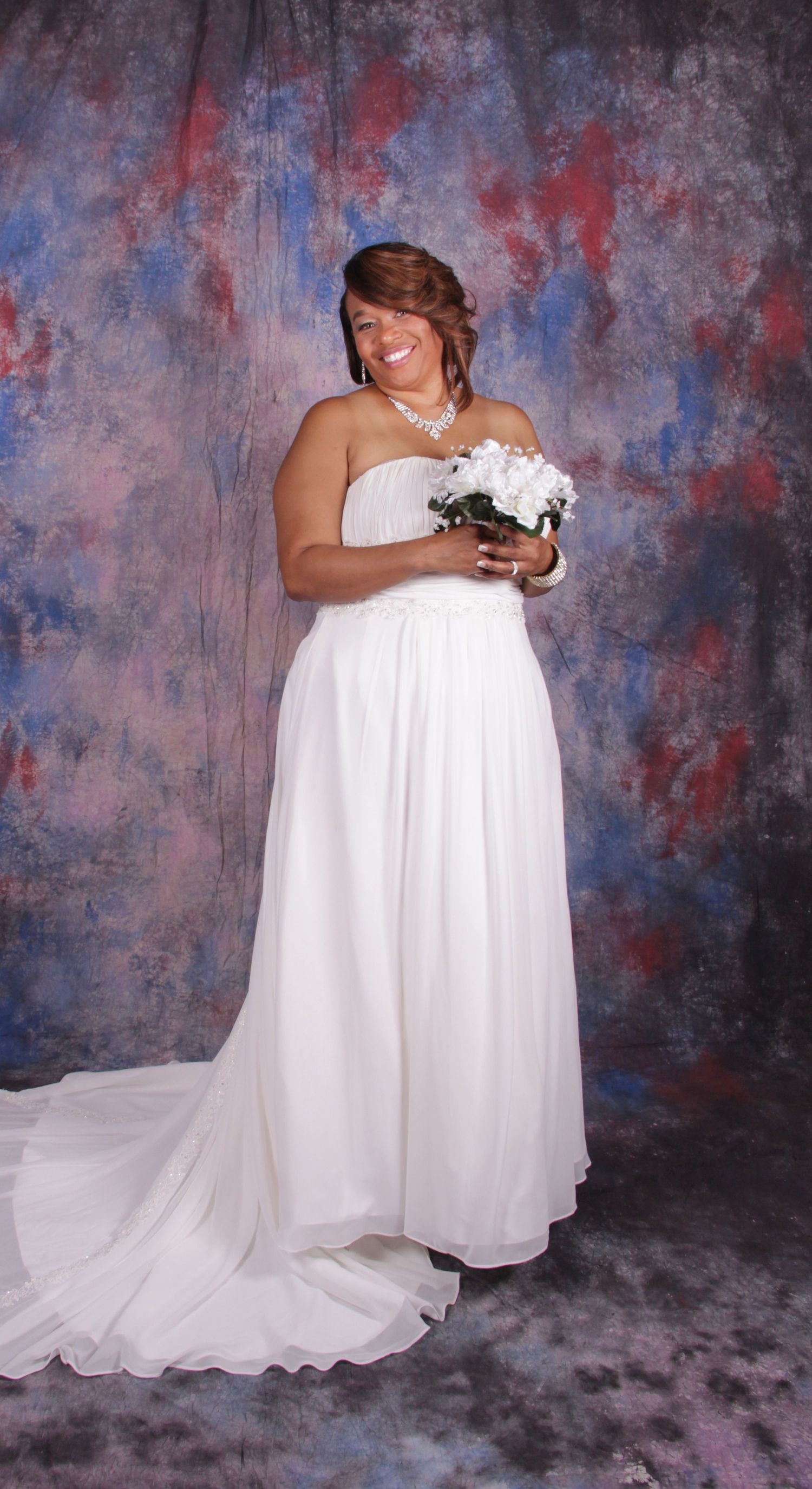 Smiling bride in strapless white wedding gown holds bouquet against colorful painted studio backdrop.