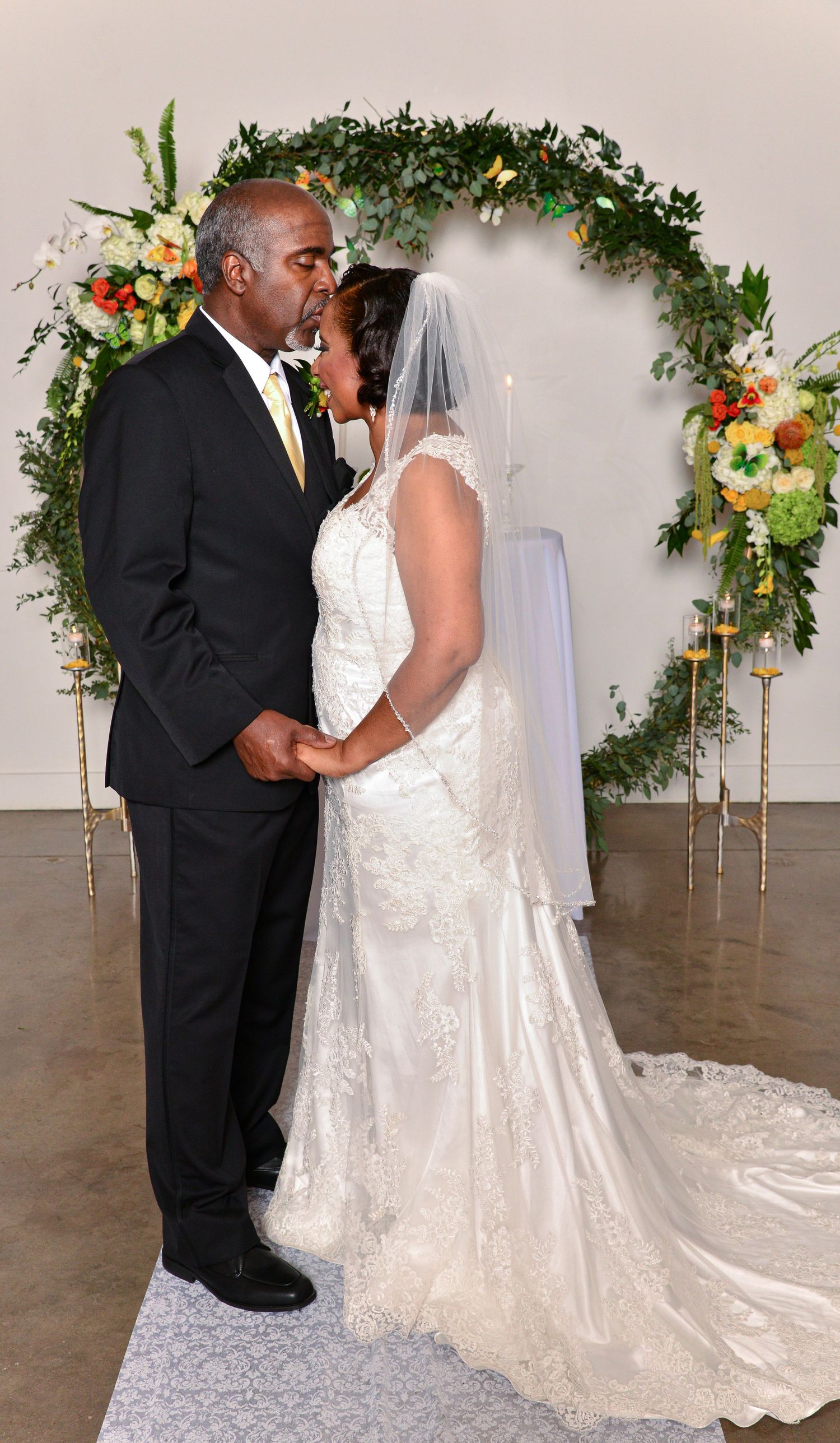 Bride and groom sharing first kiss at wedding altar decorated with lush floral arch.