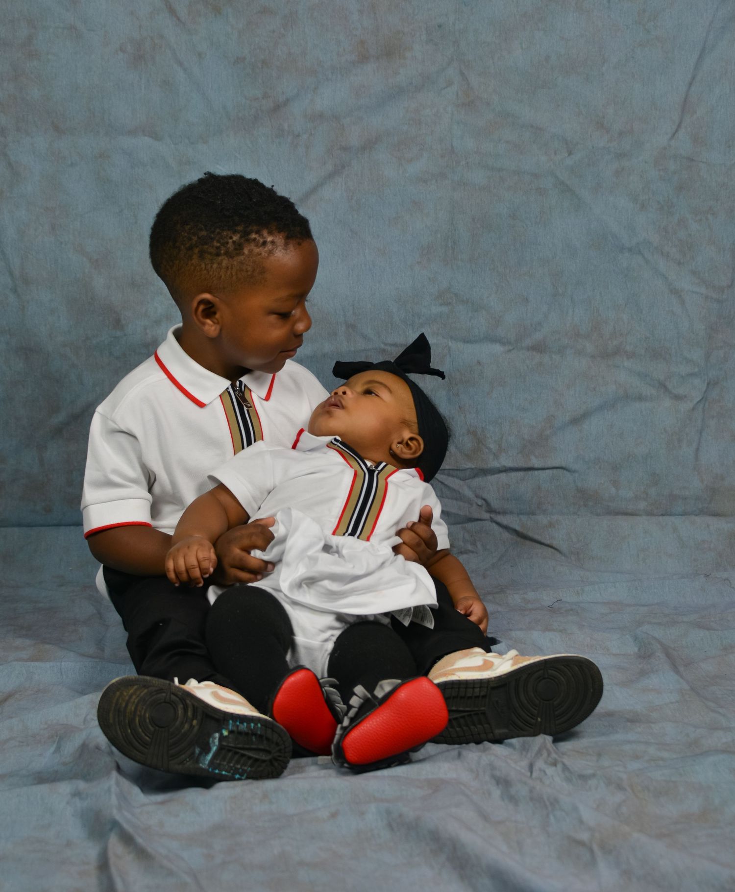 Two young siblings in matching white Burberry outfits sitting together for a portrait.