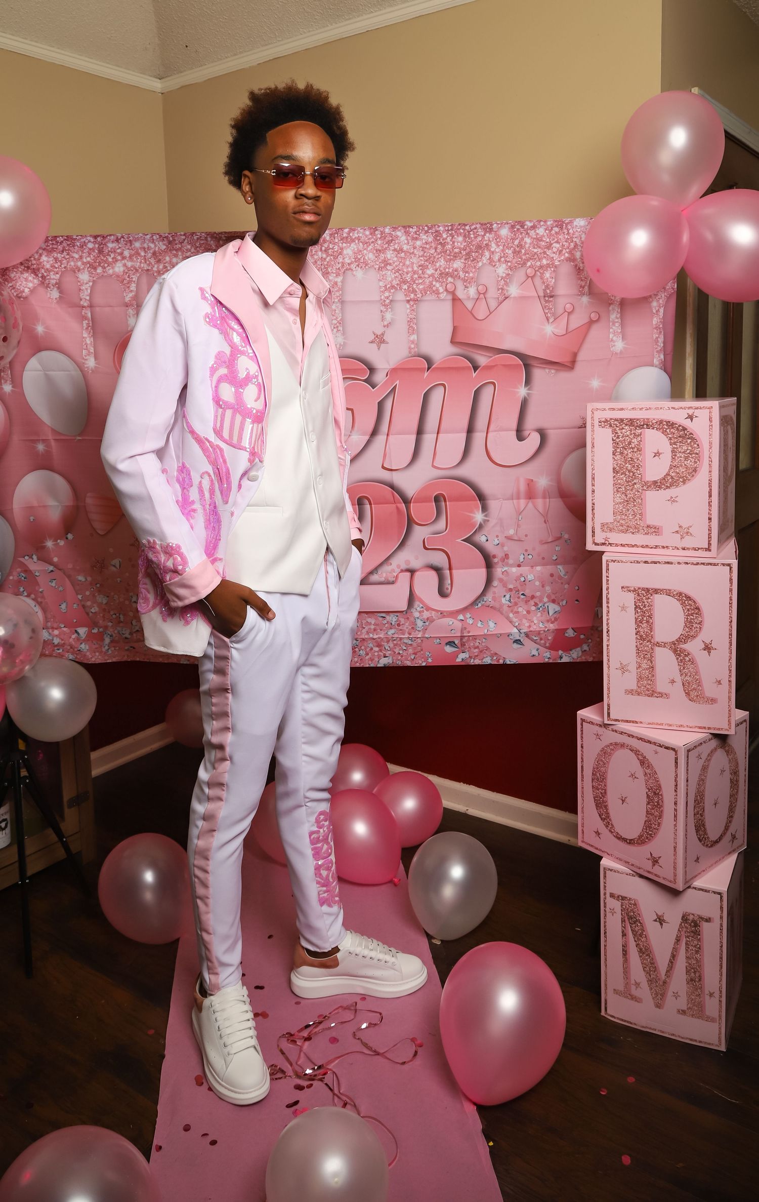 Young man in pink prom suit posing in front of Prom 23 balloon backdrop.