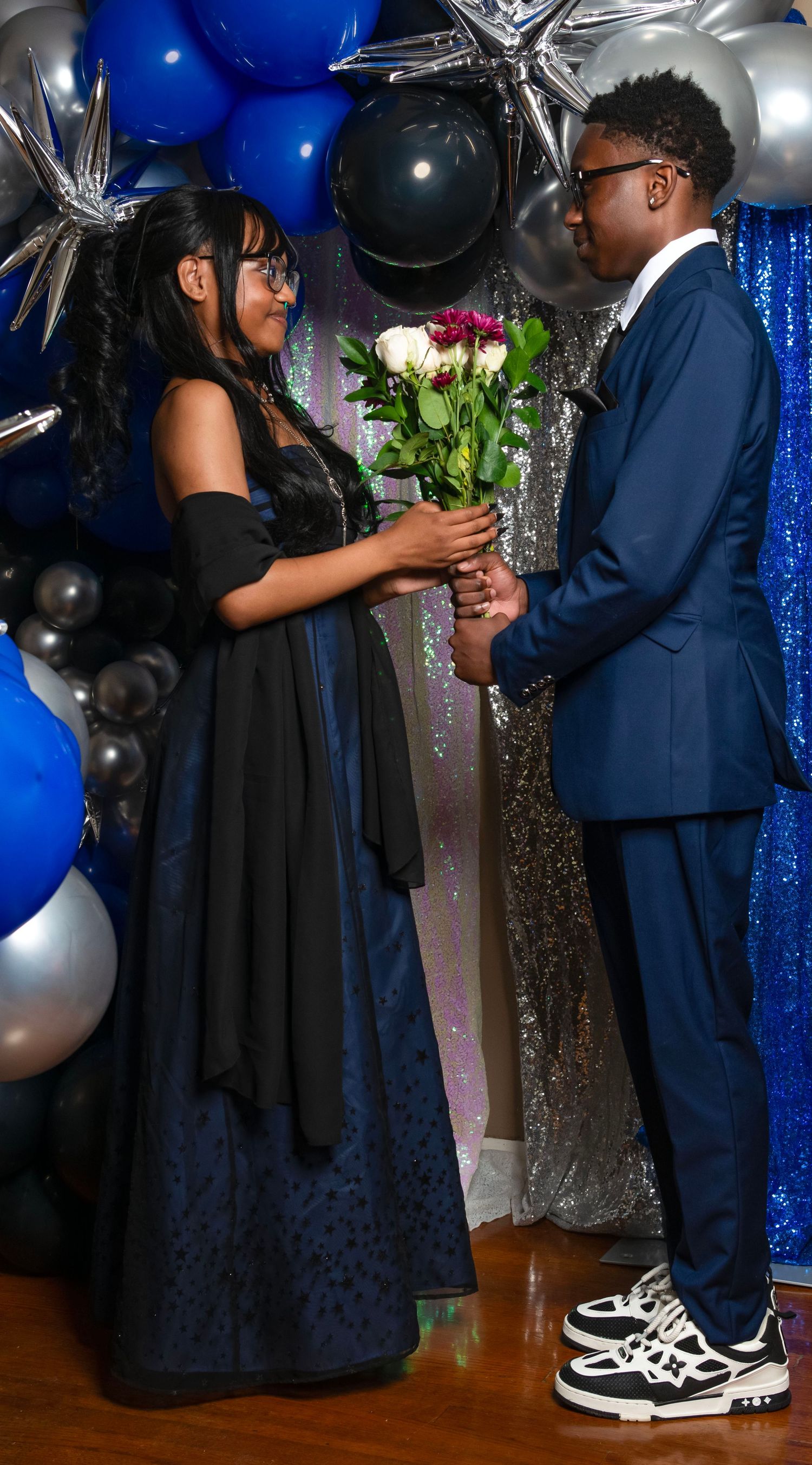 A young couple in formal attire share a moment, the man presenting roses to his date.