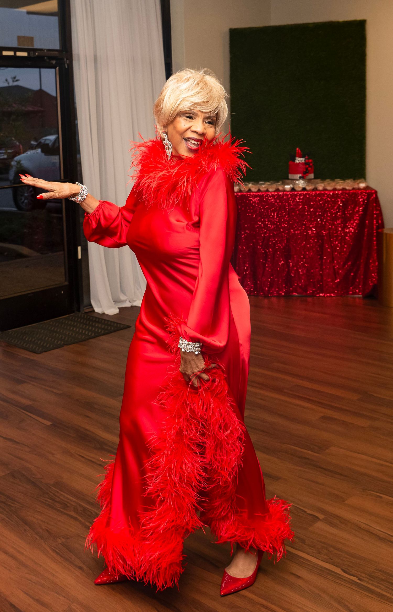 Elegant elderly woman in a stunning red feathered gown posing gracefully at a formal event.