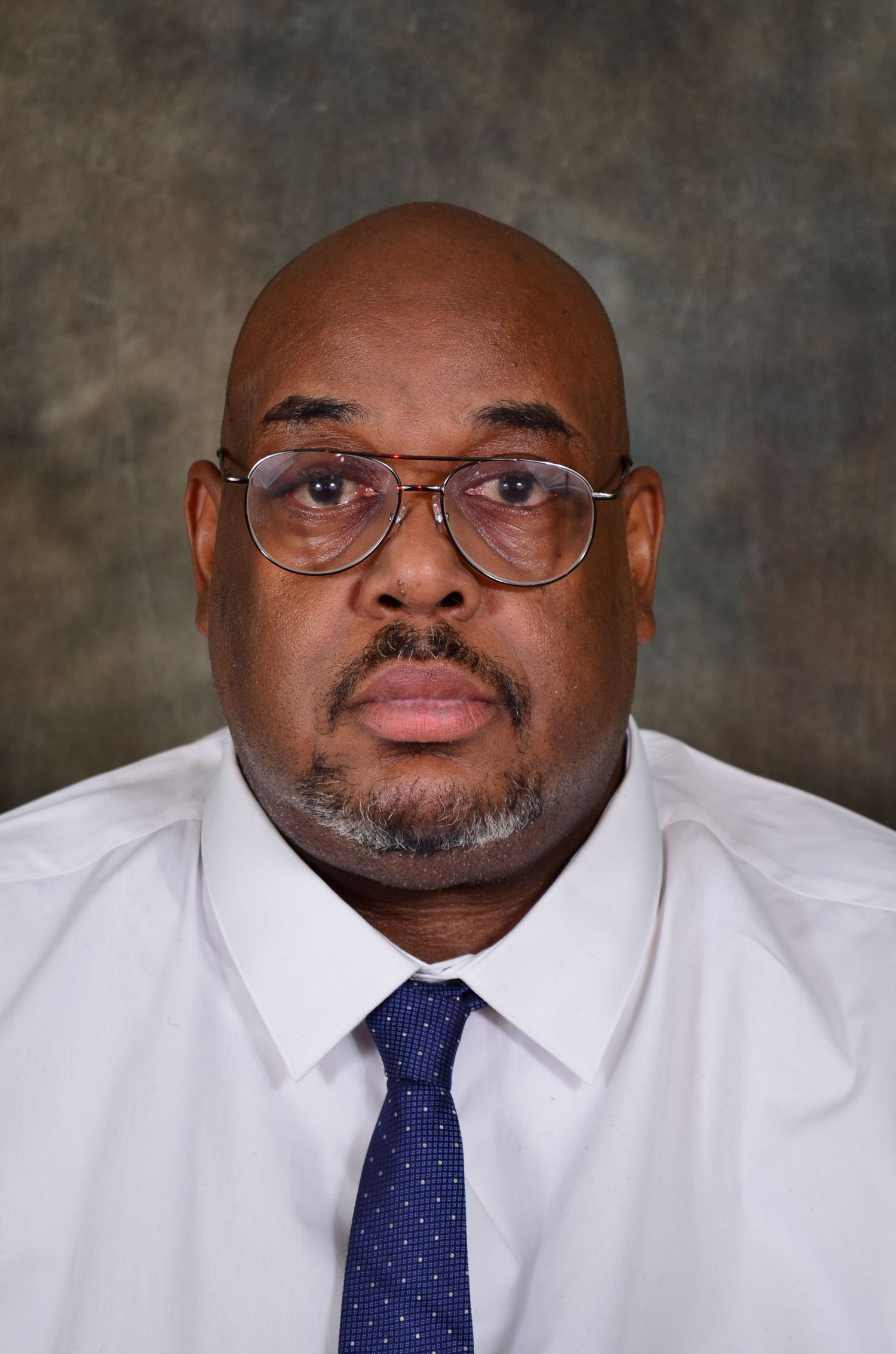 Professional headshot of  man wearing white dress shirt and blue tie.