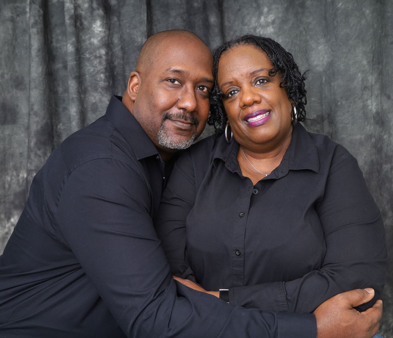 Couple in matching black shirts sharing a warm embrace in a professional studio portrait photo.