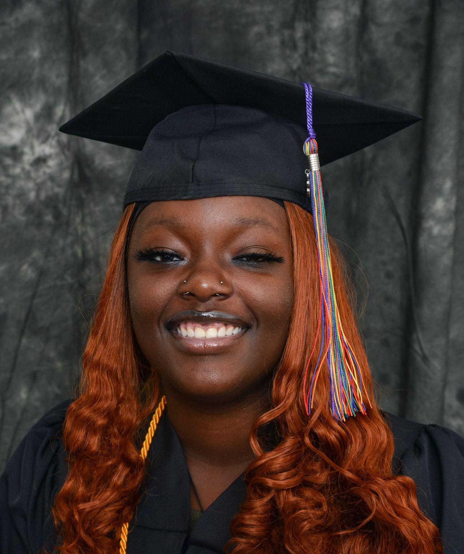 Smiling graduate in black cap and gown with colorful tassel portrait photo.