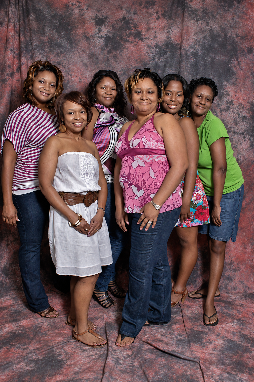 Six women posing together for a group portrait photo against a mottled red backdrop.
