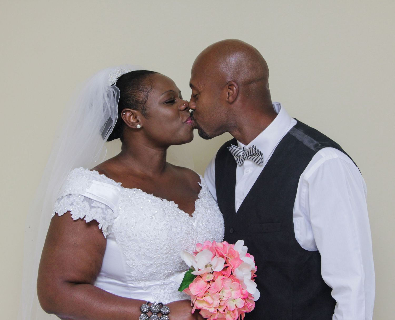 Bride and groom sharing a kiss while holding pink peony bouquet at wedding.