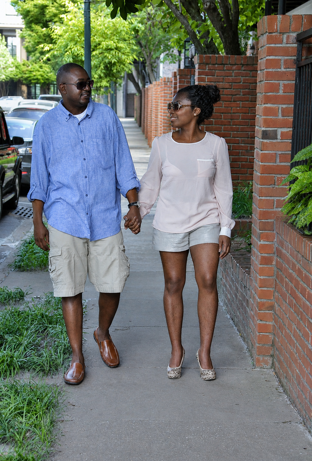 Couple walking hand-in-hand on a sunny urban sidewalk in casual summer attire.