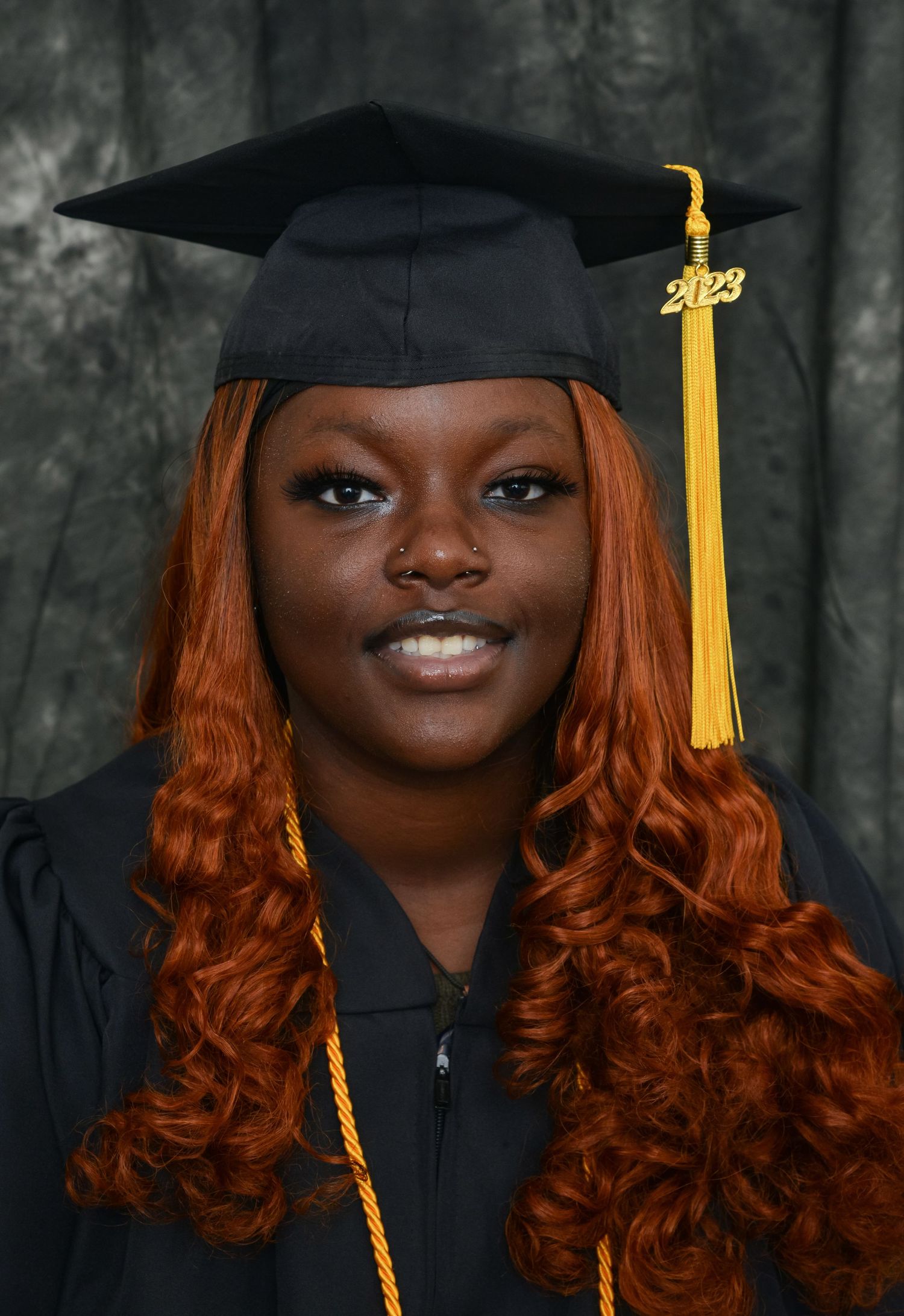 Graduate in black cap and gown with gold honor cord and 2023 tassel poses for portrait photo.