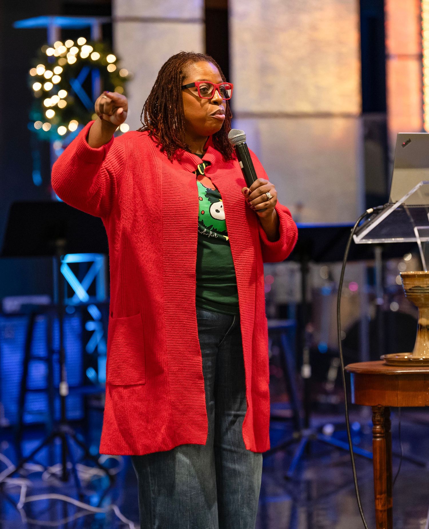 Woman in red coat and green shirt speaking at church event with microphone.