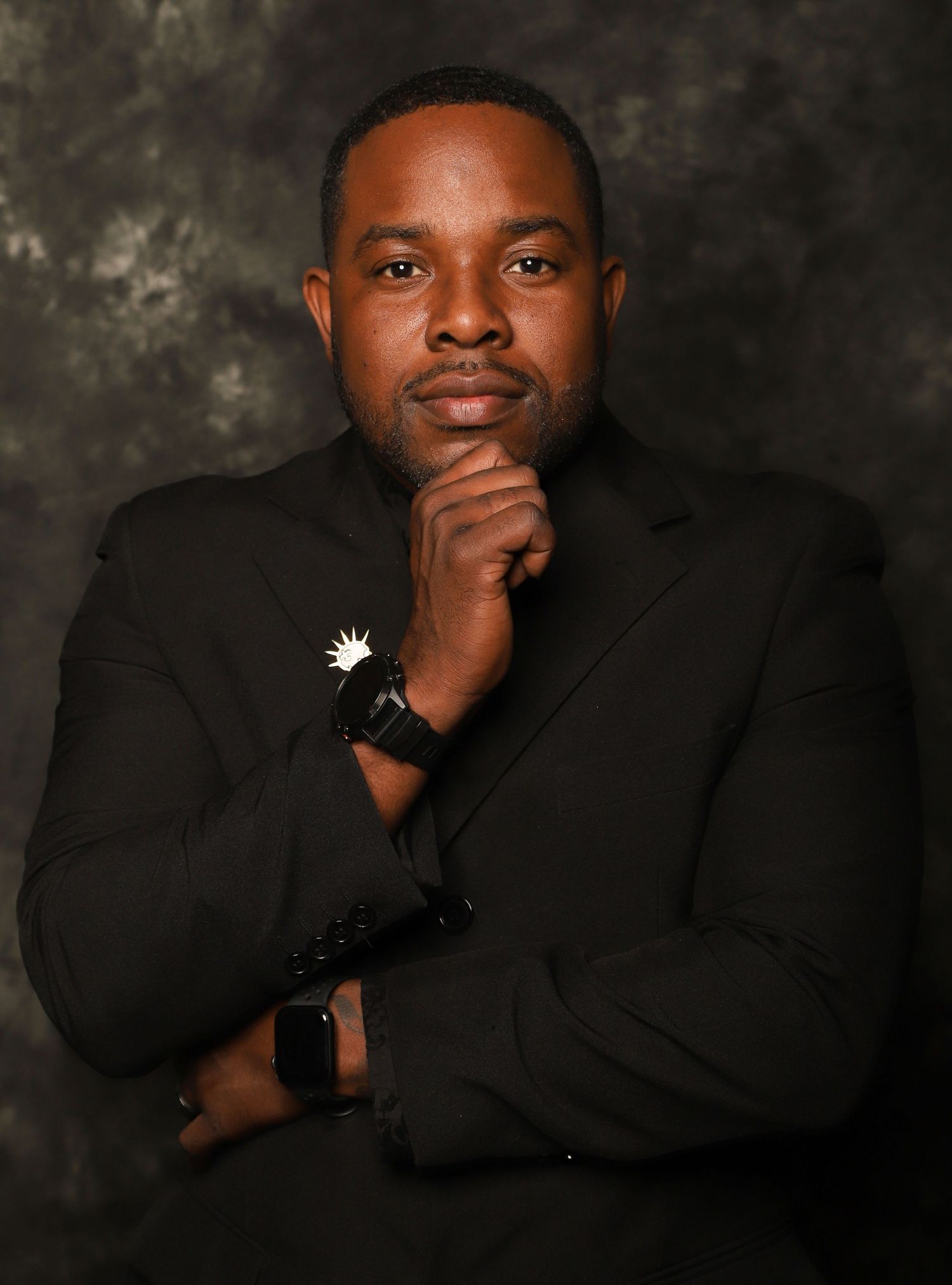 Professional man in black suit posing thoughtfully for formal portrait photo.