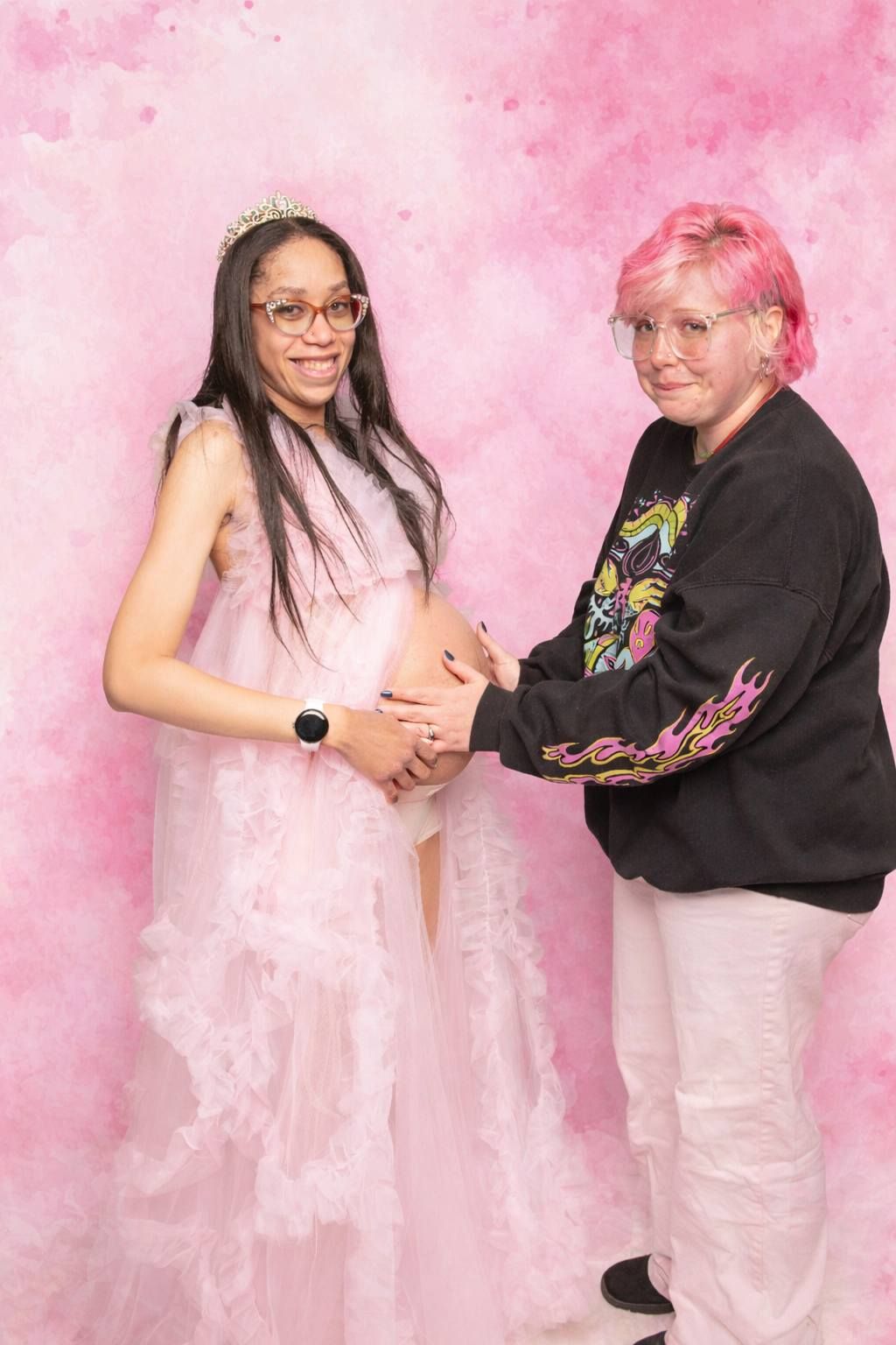 Pregnant woman in pink maternity gown with tiara posing with partner at a baby shower.