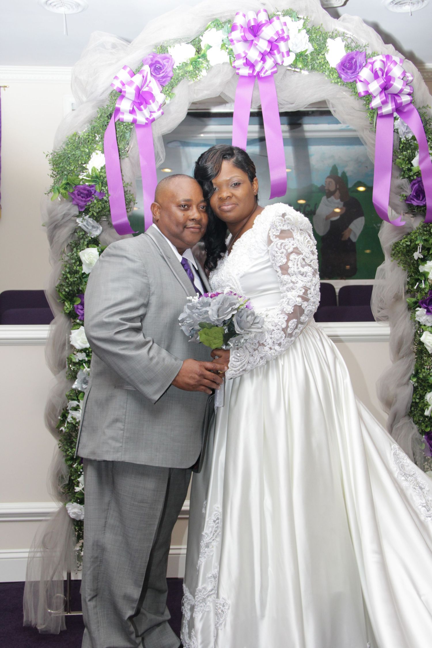 Couple posing at wedding altar decorated with purple and white floral arch.