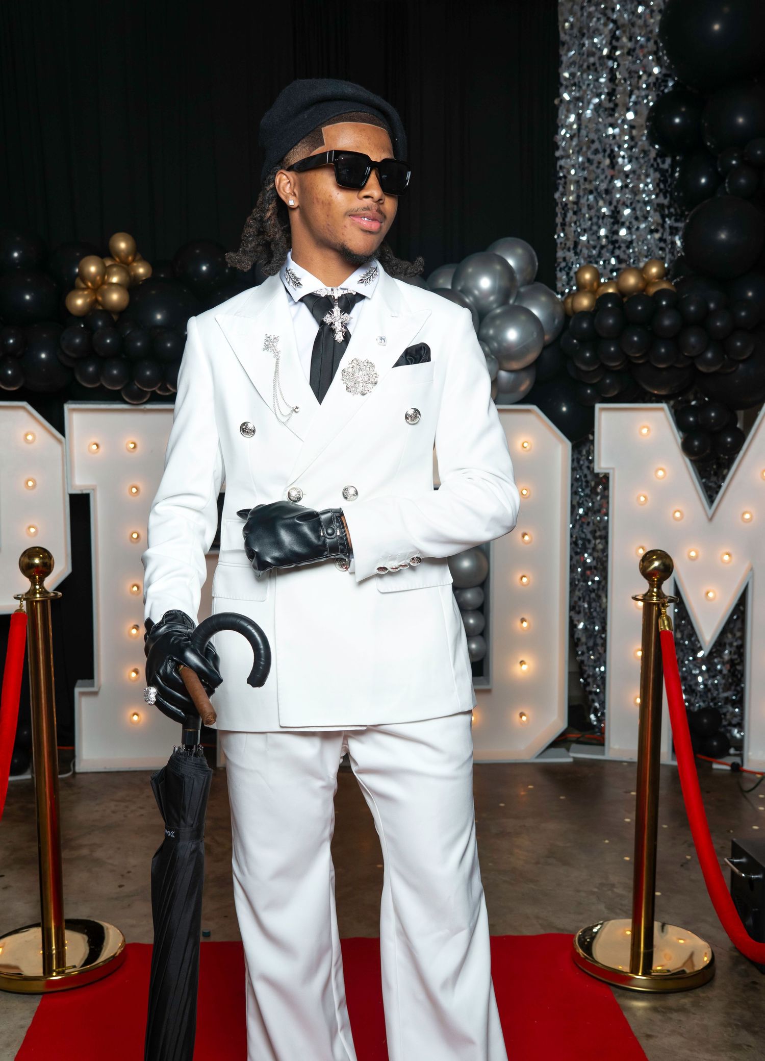 Fashionable teen in white double-breasted suit with beret and sunglasses at prom event.