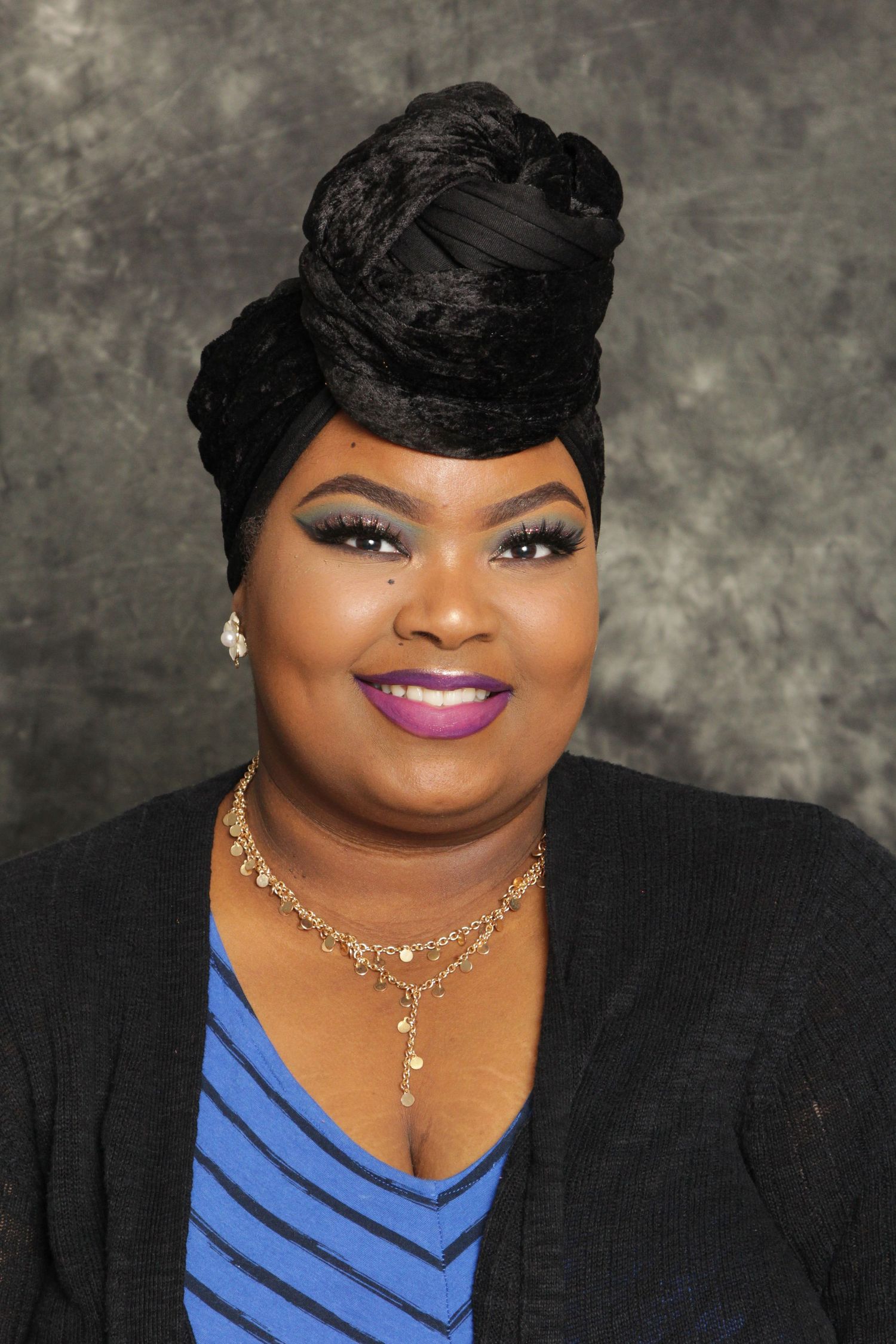 Confident woman wearing decorative black head wrap and blue striped top with purple lipstick.