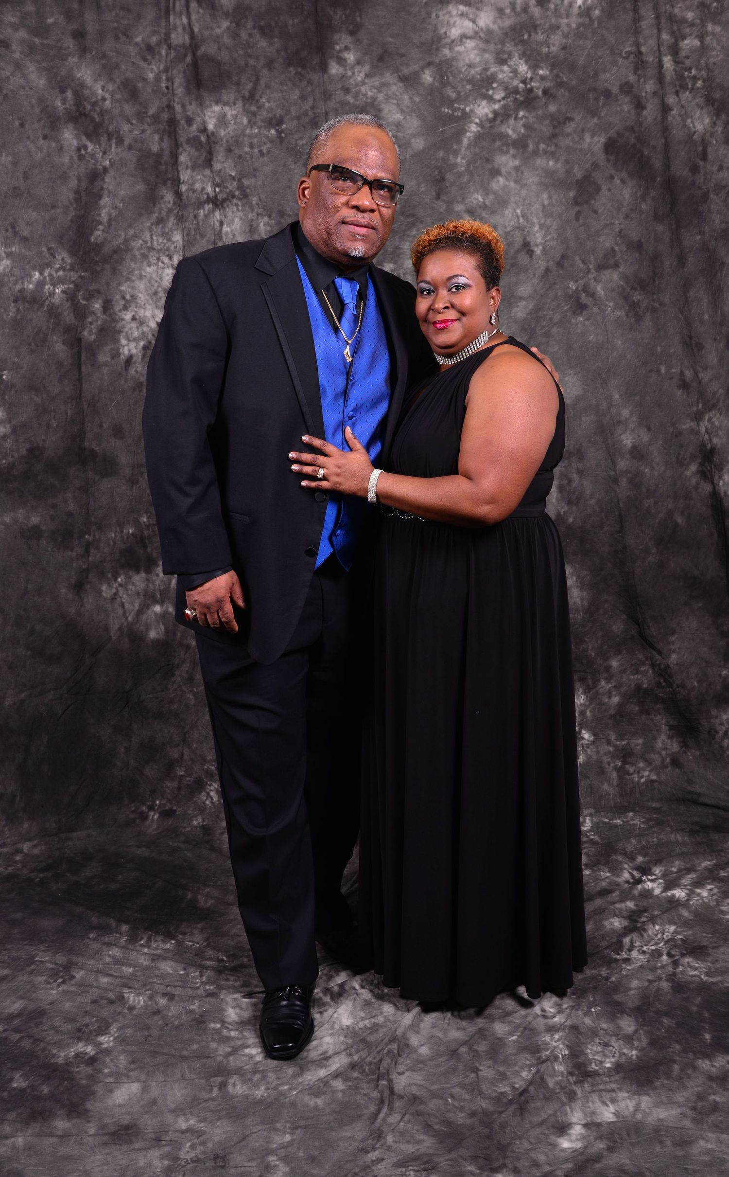 Elegant couple in formal black attire with blue accents posing for a professional studio portrait photo.