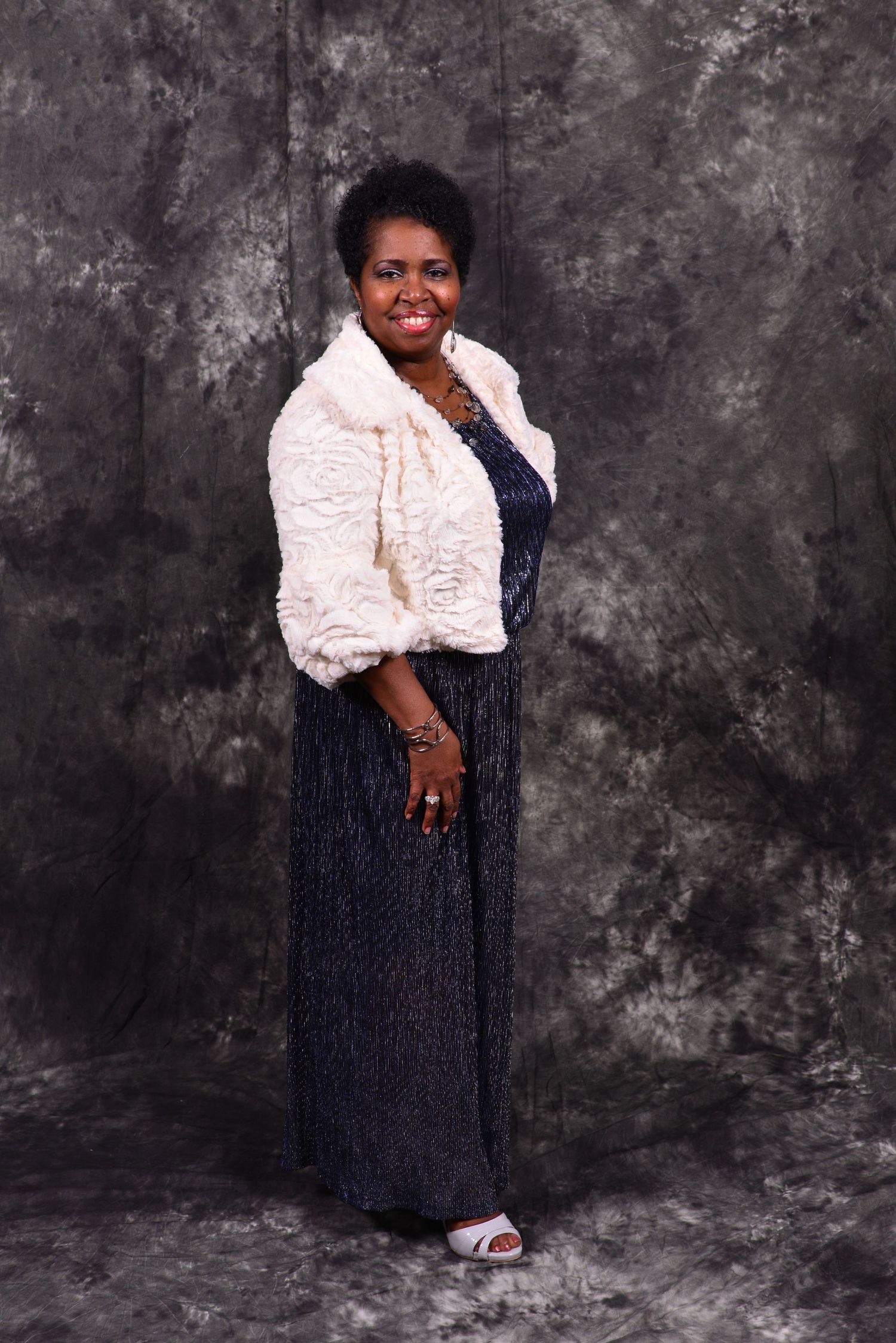 Woman posing gracefully in navy sequin gown with white fur jacket in formal studio portrait.