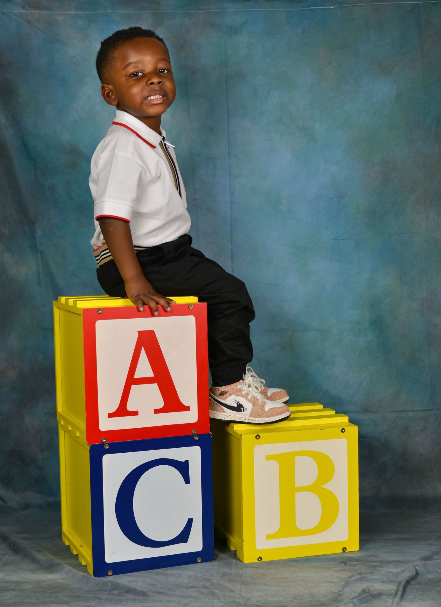Young boy in school uniform sits atop colorful ABC alphabet blocks in studio portrait.