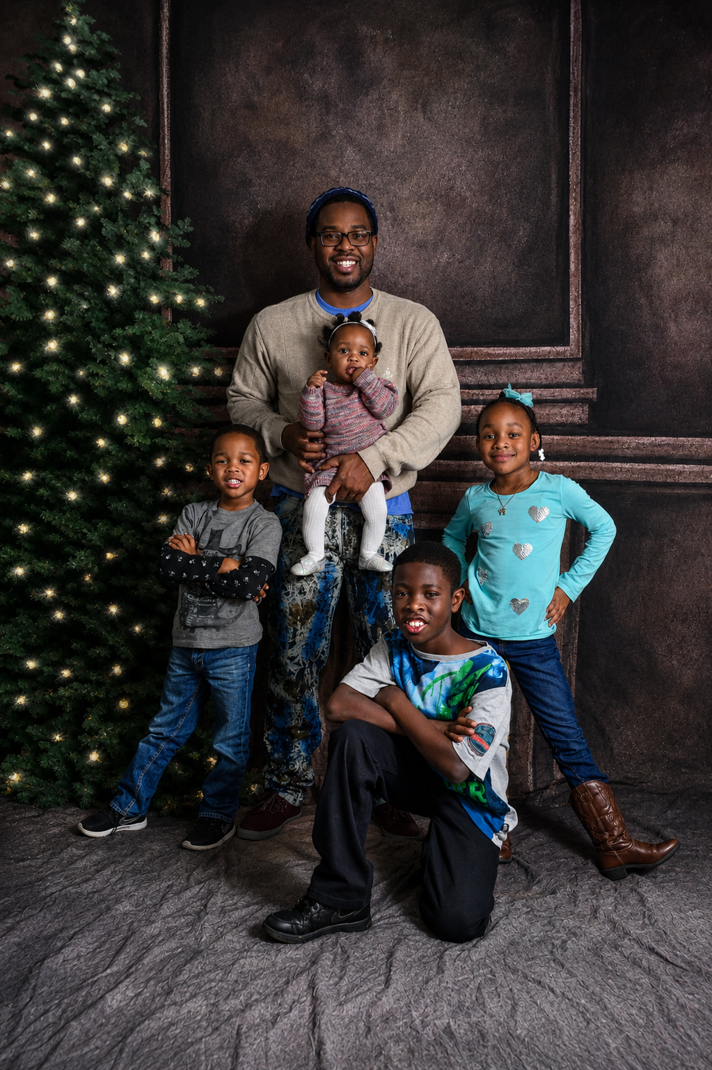 Family holiday portrait with father and four children posing near lit Christmas tree.
