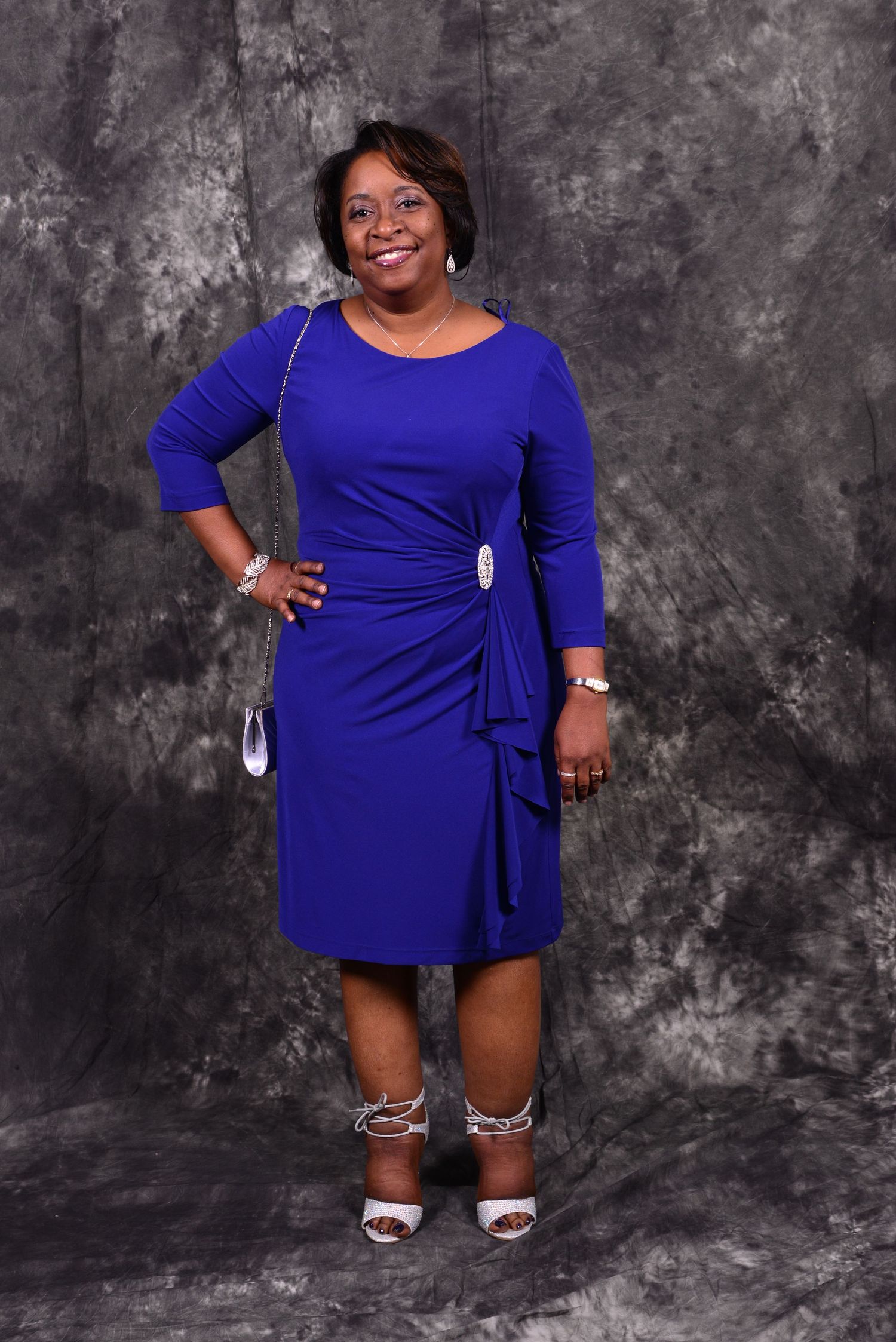 Smiling woman posing confidently in royal blue dress with silver accessories in studio portrait.