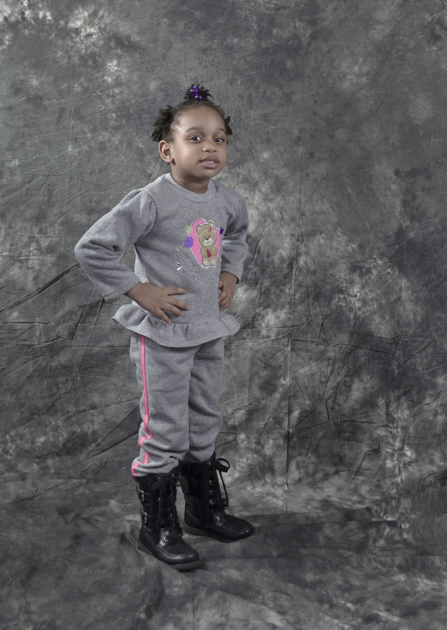 Young girl posing confidently in gray tracksuit and black boots against studio backdrop.