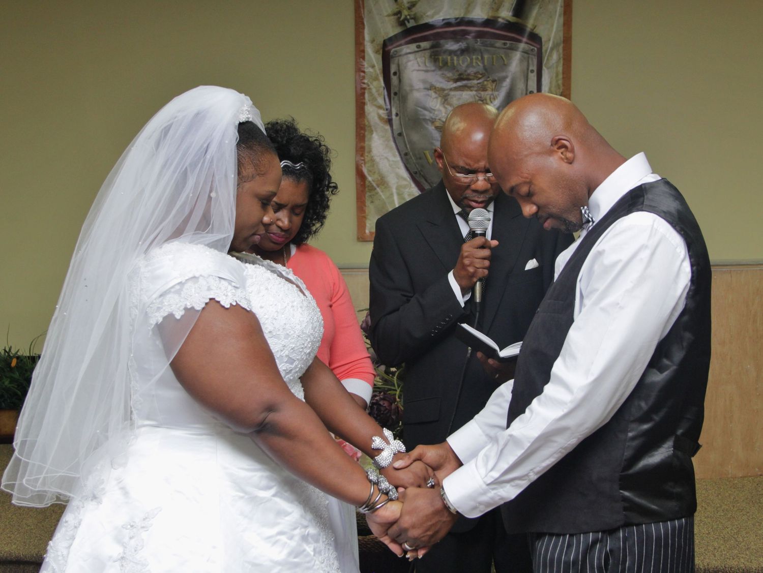 Bride and groom holding hands in prayer during wedding ceremony with officiant.