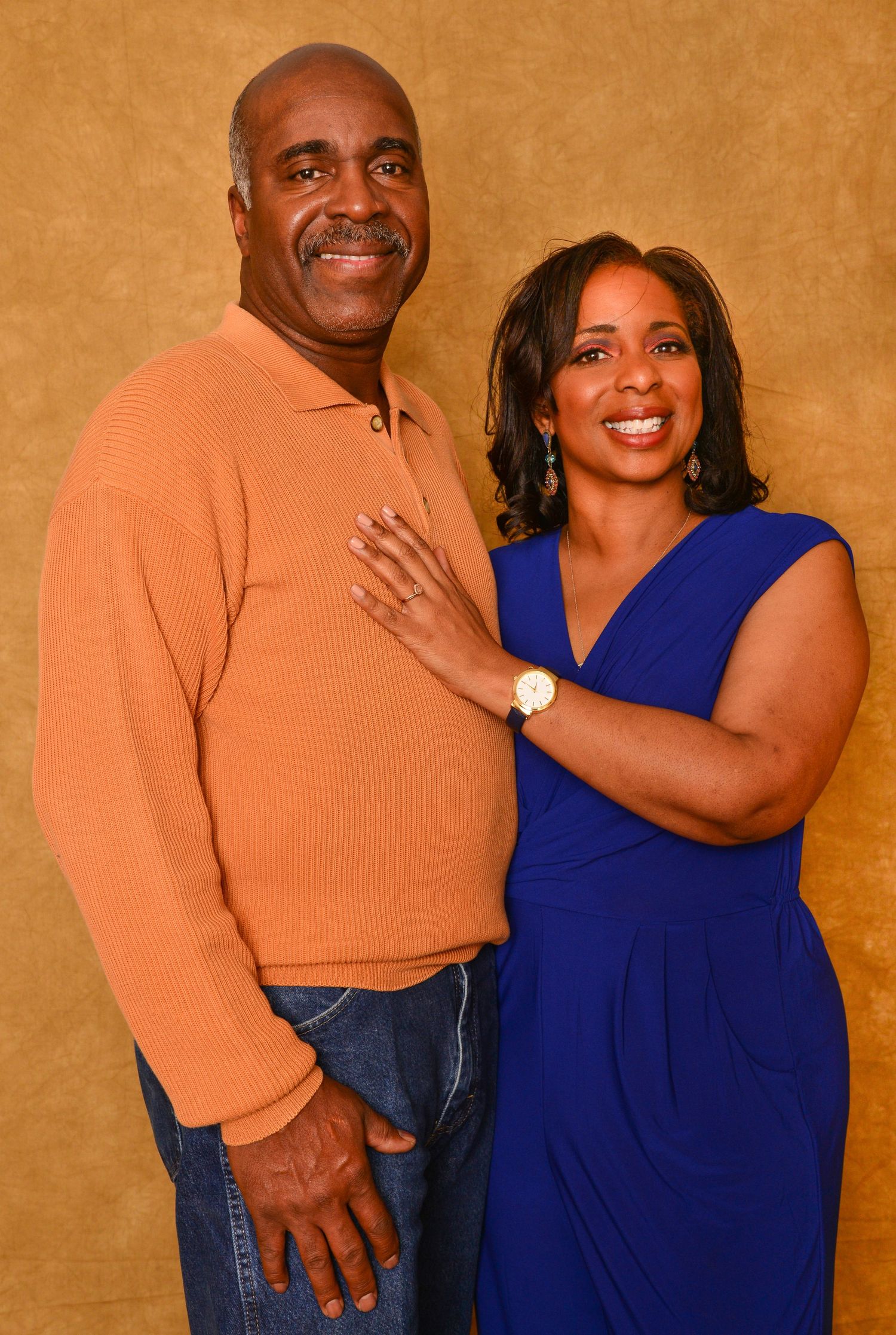 Smiling couple posing together, man in orange sweater and woman in blue dress, in a professional portrait.