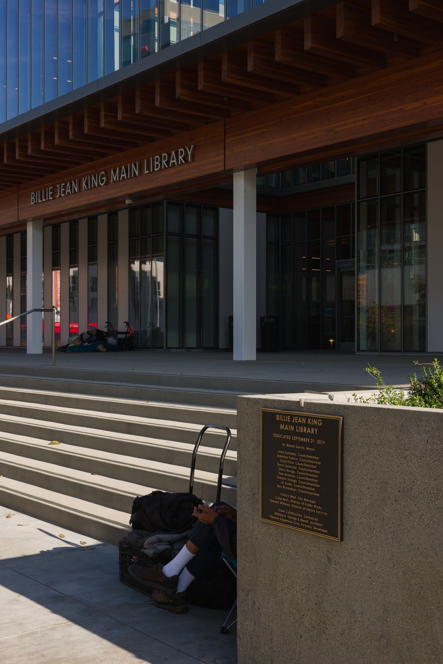A homeless person smoking at the steps of the Billie Jean King Main Library
