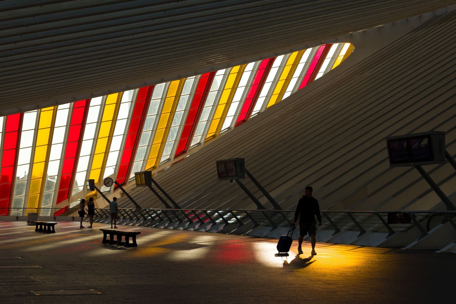Interior of Liège-Guillemins train station, Santiago Calatrava, Belgium. Travelers backlit with colorful art installation by Daniel Buren.