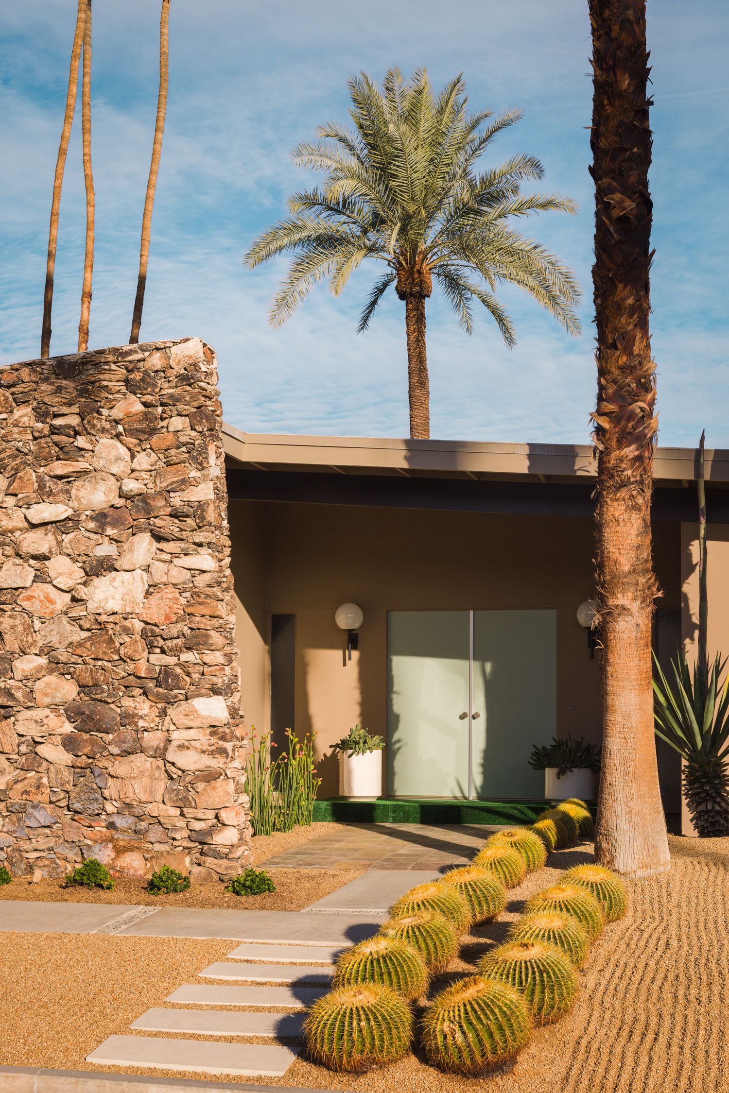 barrel cactus lined entry to a MCM home in Palm Springs with a stacked stone fireplace