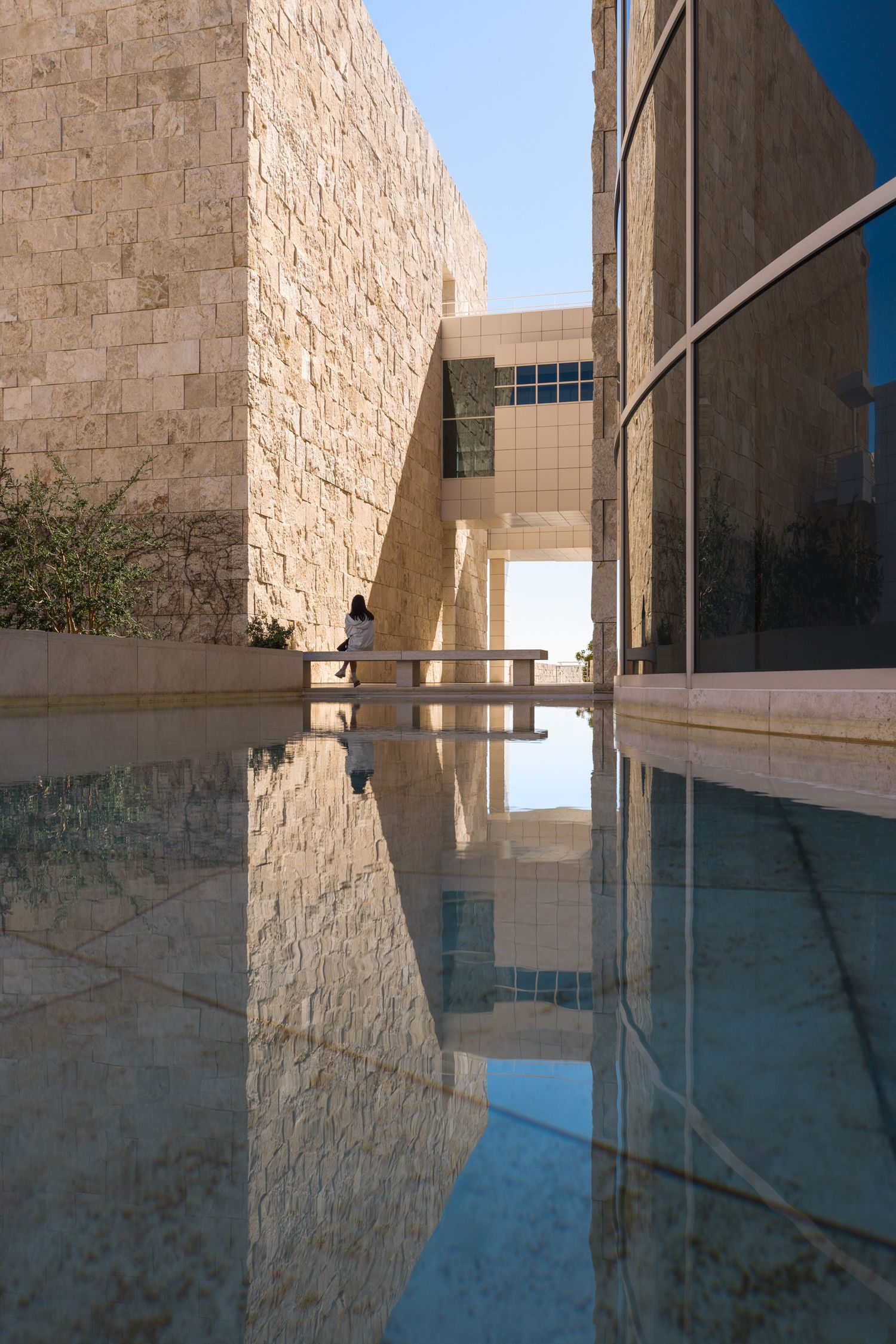 A seated lone woman and surrounding architecture reflected in a fountain at the Getty Center by Richard Meier in Los Angeles