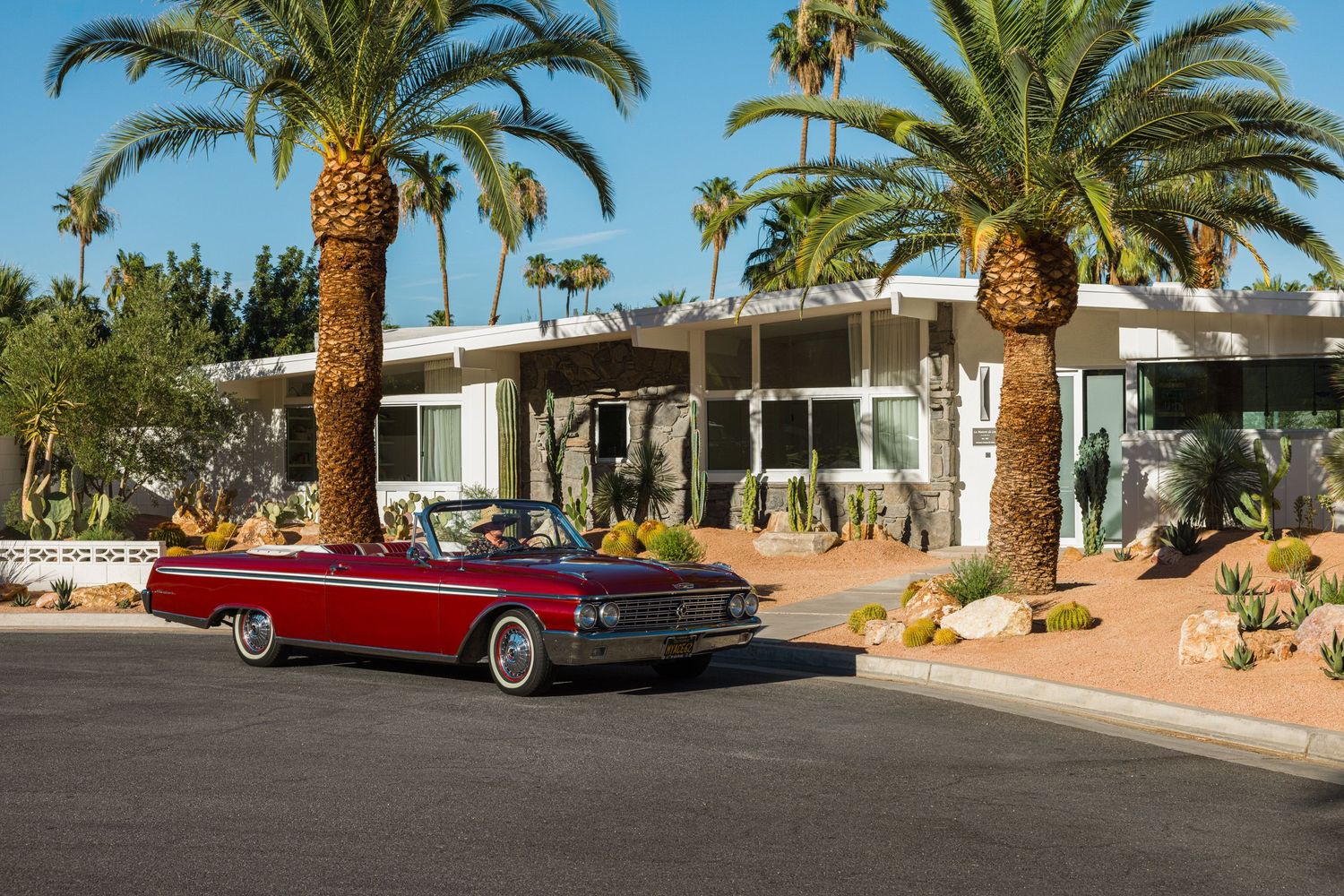 Matt Sorum driving a 1962 Ford Galaxie 500 XL Sunliner convertible in Rangoon Red in front of a mid-century modern home in Palm Springs