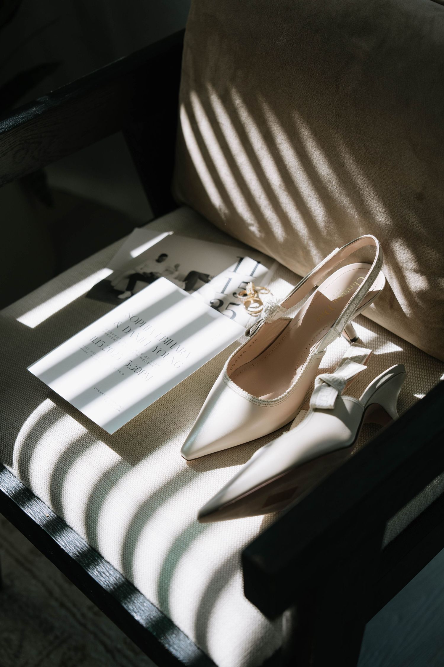 Elegant bridal heels and wedding rings on chair with dramatic striped sunlight shadows.