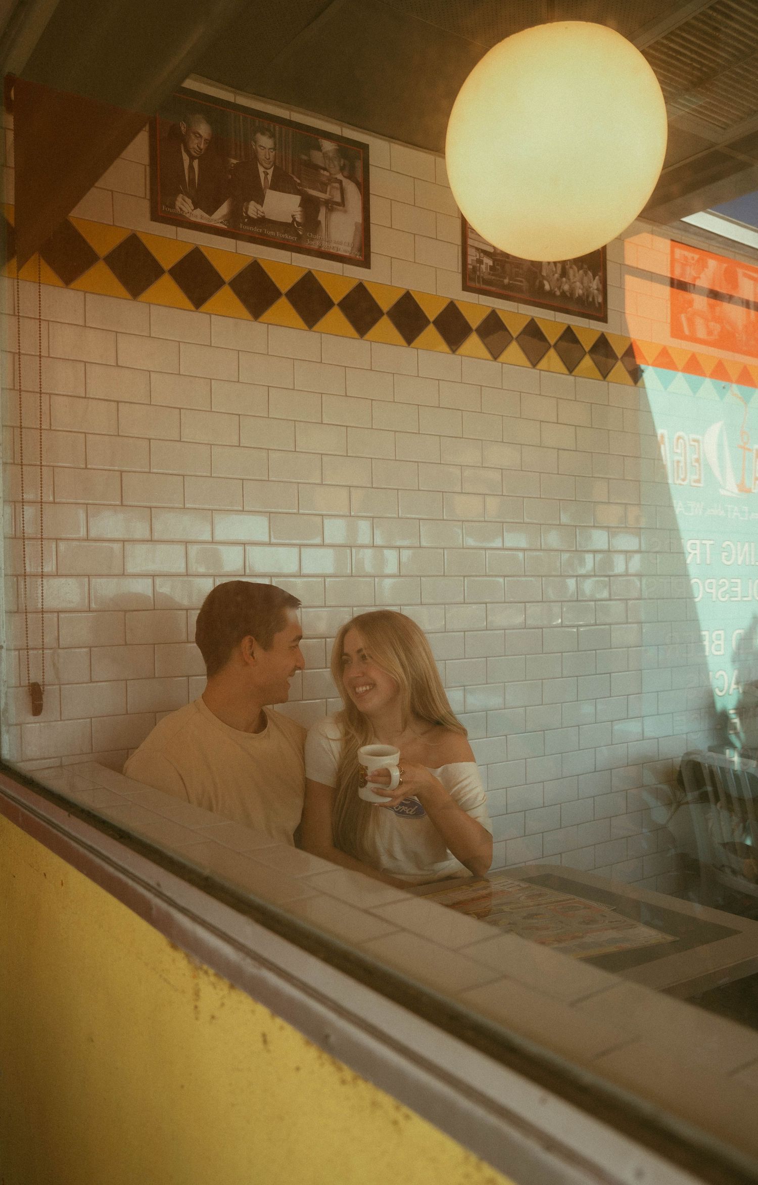Young couple smiling at each other in a retro diner booth, sharing drinks together.