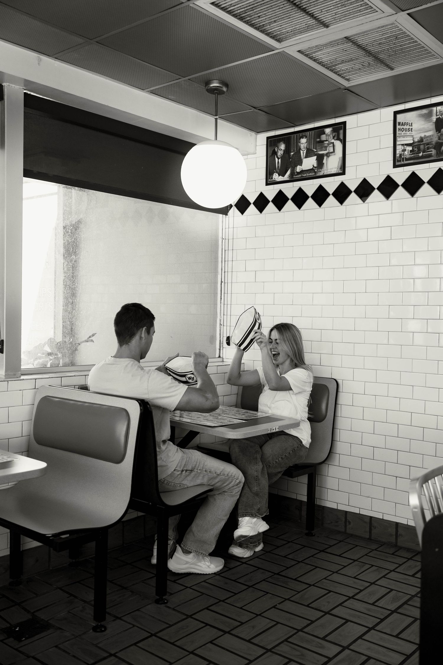 Black and white photo of playful couple laughing together in a classic retro diner booth.